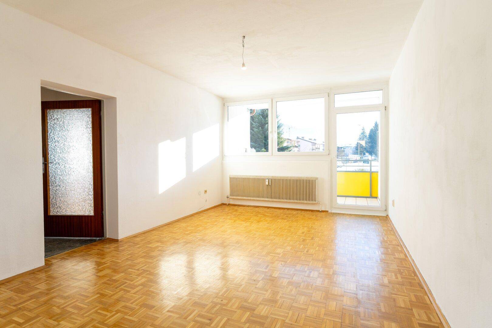 Helles Wohnzimmer mit Parkettboden und direktem Zugang zu einem Balkon.