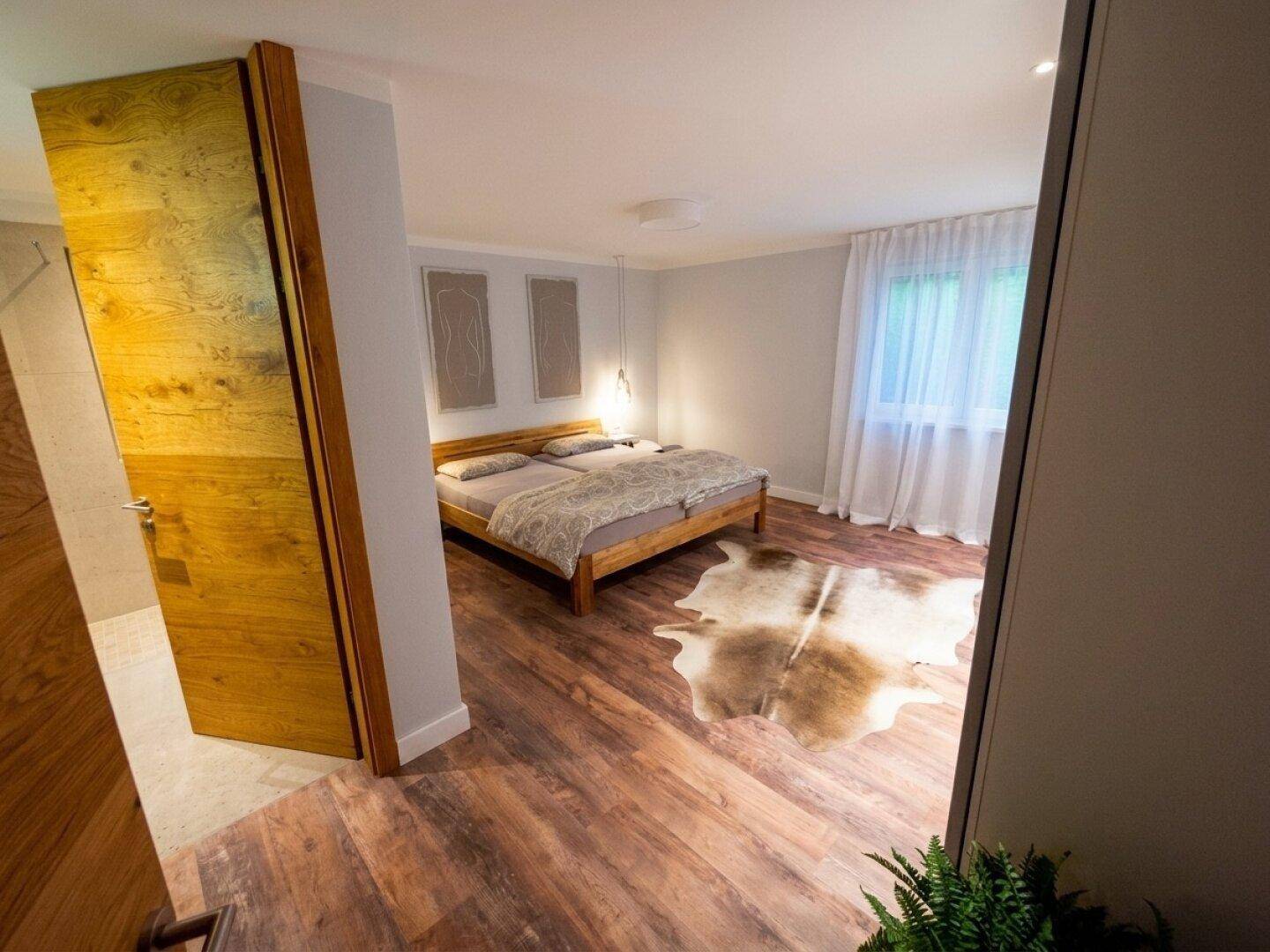 Gemütliches Schlafzimmer mit Holzboden, Doppelbett und Fenster mit Vorhängen.