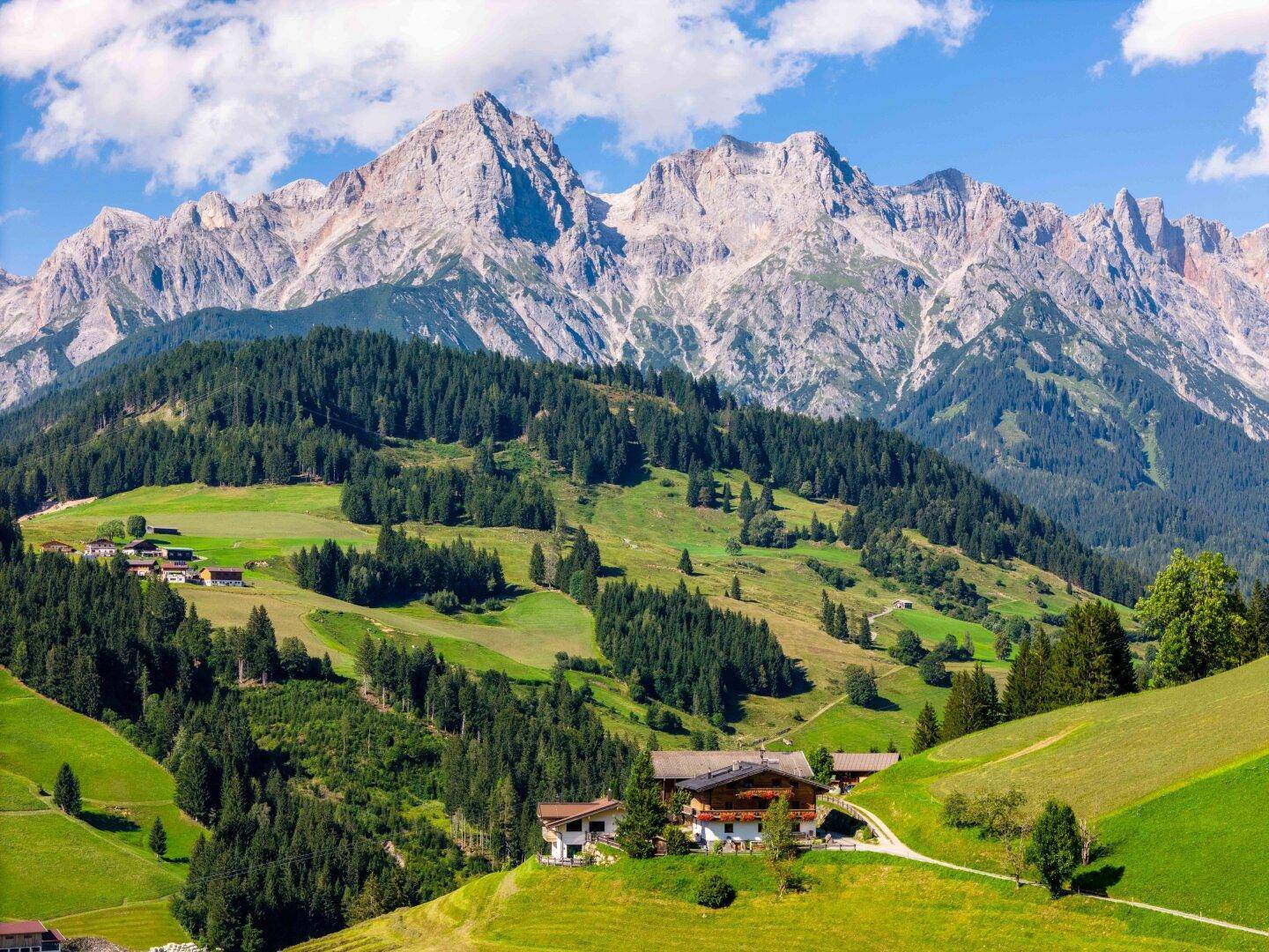 Malerische Berglandschaft im Sommer mit grünen Wiesen, Wäldern und traditionellen Häusern.