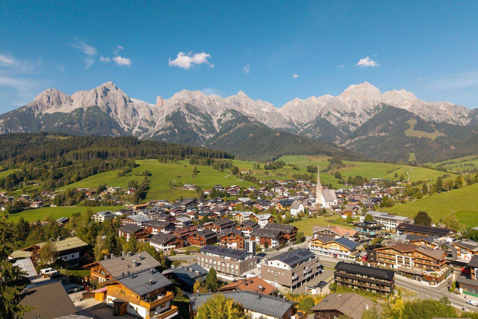 Malerische Alpenstadt mit traditionellen Häusern und beeindruckendem Bergpanorama unter blauem Himmel.