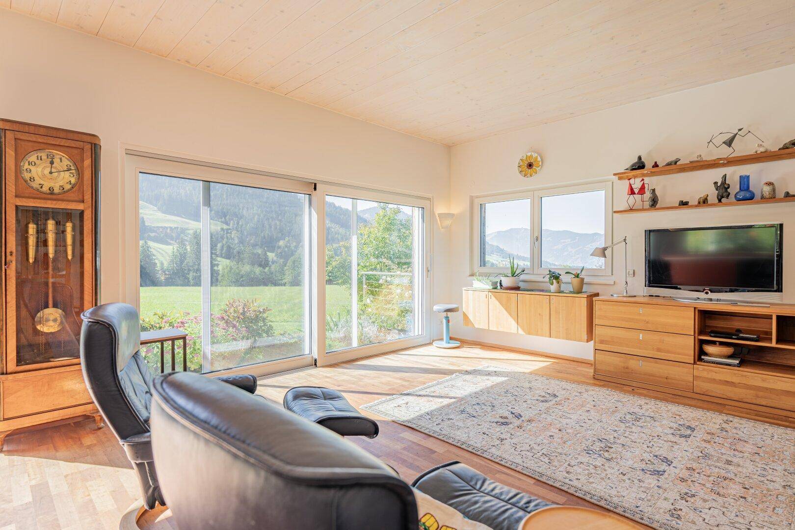 Helles Wohnzimmer mit Holzboden, großen Schiebetüren und weitem Blick auf die grüne Landschaft.
