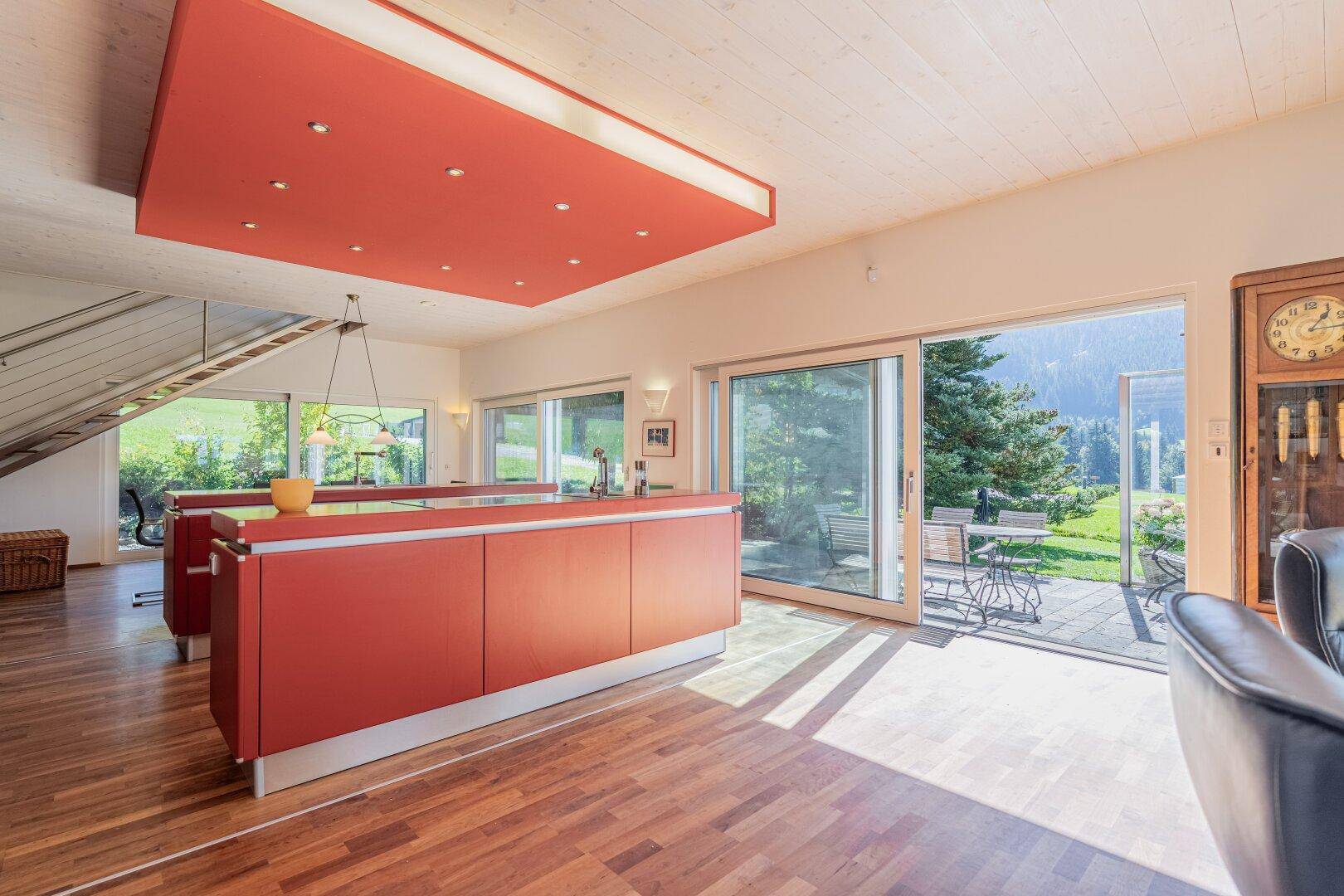 Moderne rote Küche mit Kochinsel und direktem Zugang zur Terrasse mit Gartenblick.