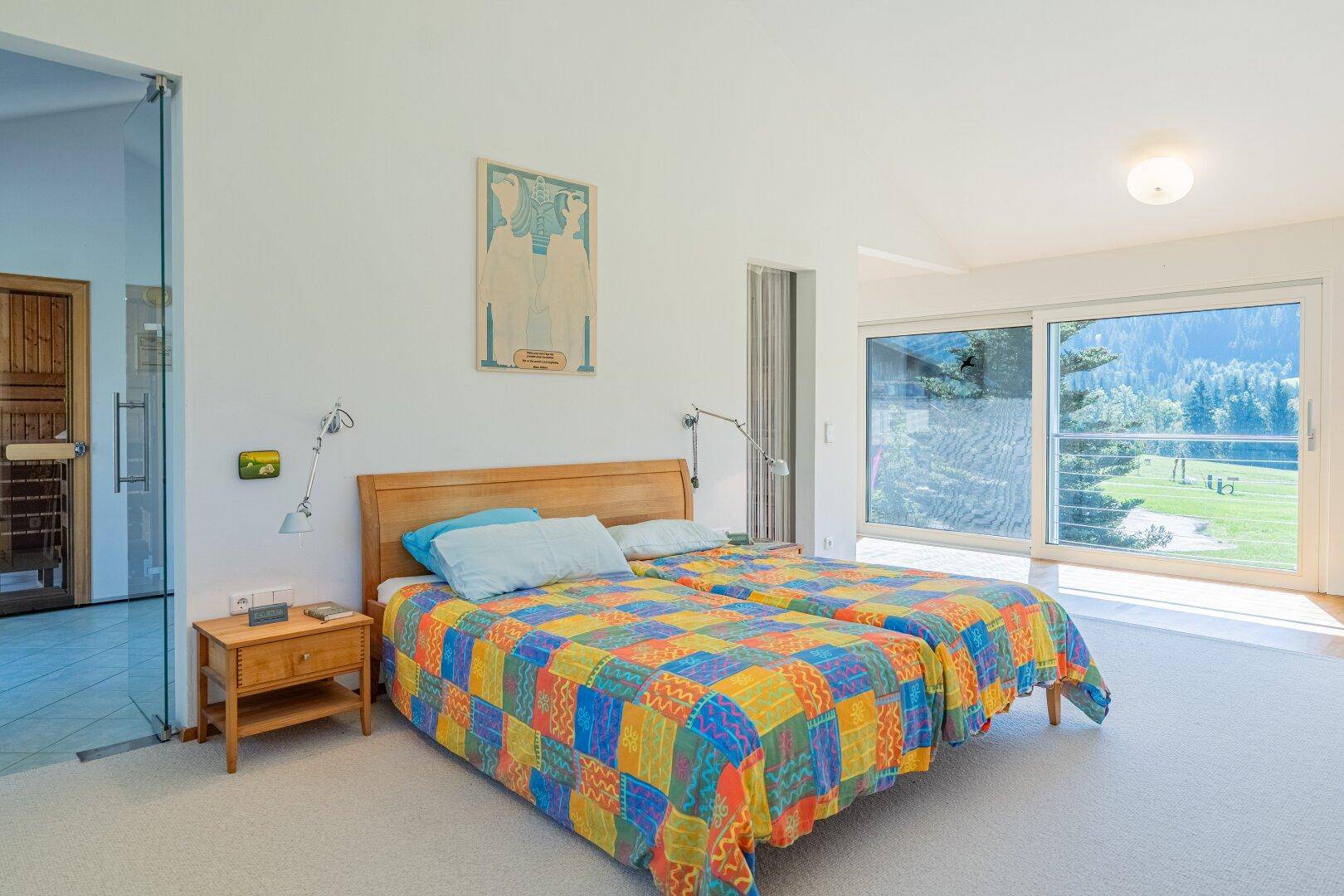 Helles Schlafzimmer mit zwei Einzelbetten, farbenfroher Bettdecke und Panoramablick ins Grüne.