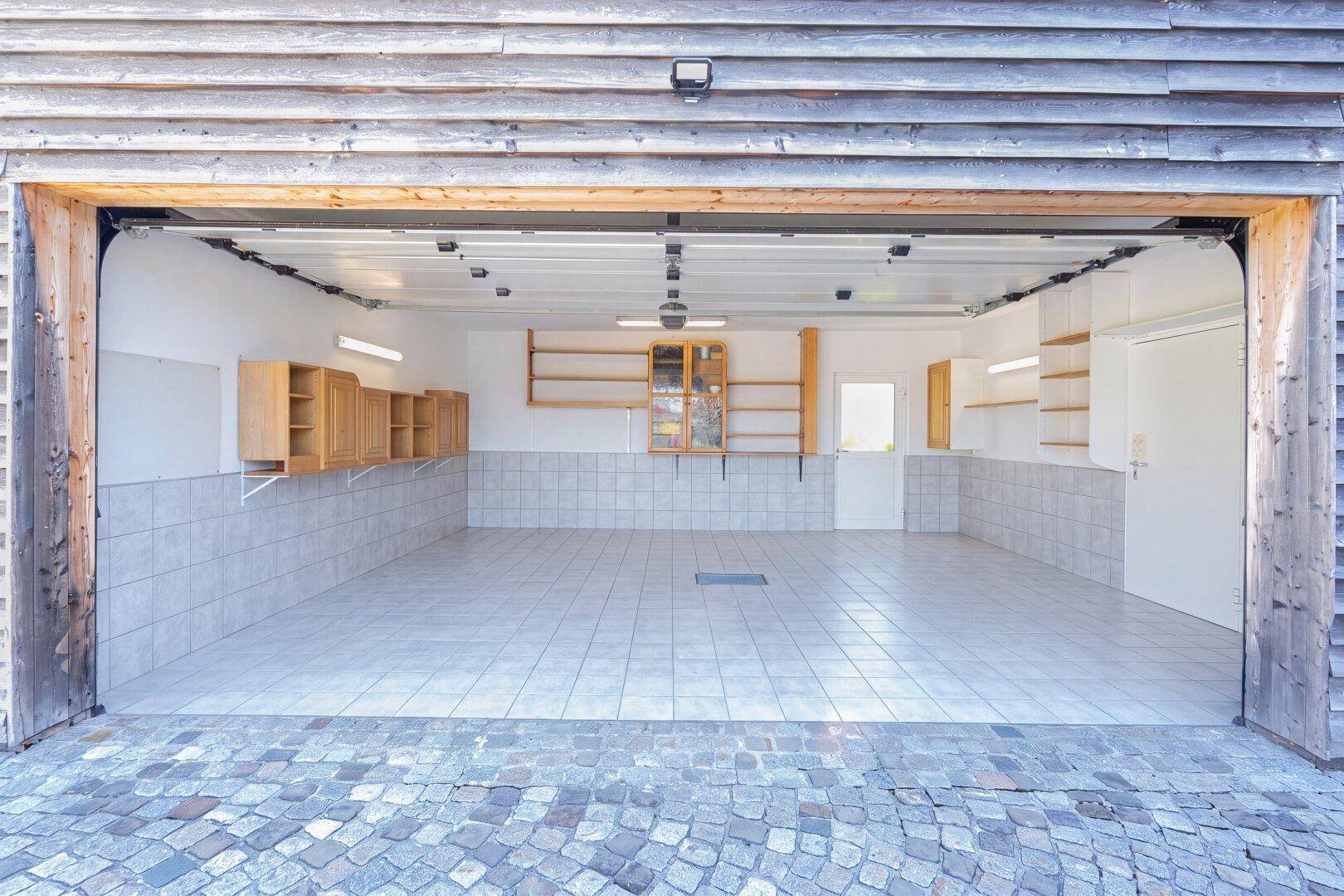Geräumige Garage mit Fliesenboden und Regalen, bietet viel Stauraum.