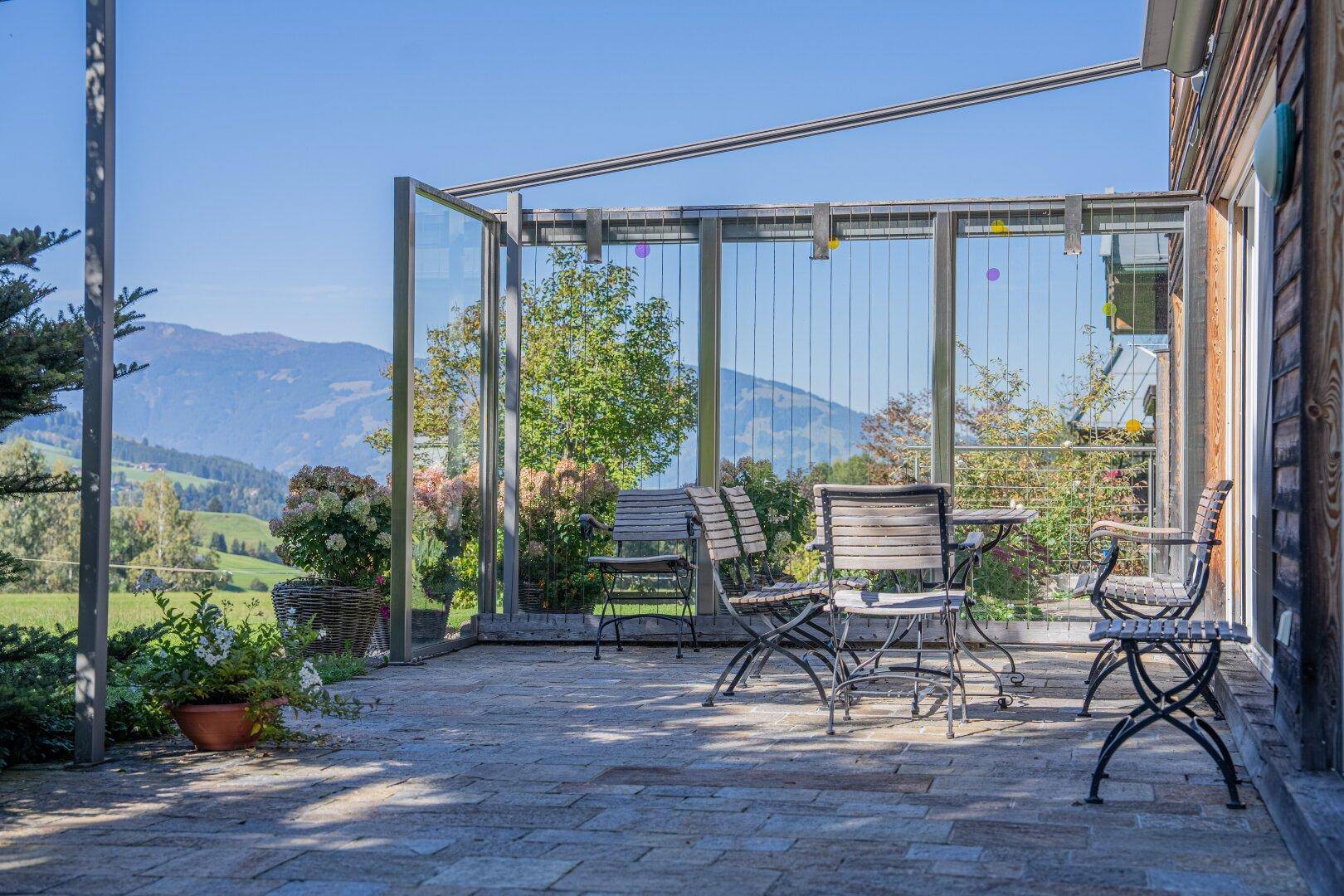 Gemütliche Terrasse mit Gartenmöbeln und Glaswindschutz, bietet einen weiten Bergblick.