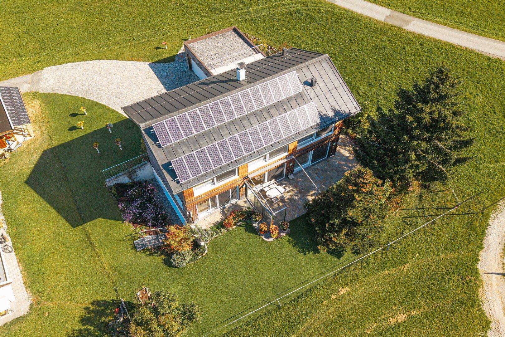Dach des Holzhauses mit Photovoltaikanlage und gepflegtem Gartenbereich in sonniger Umgebung.