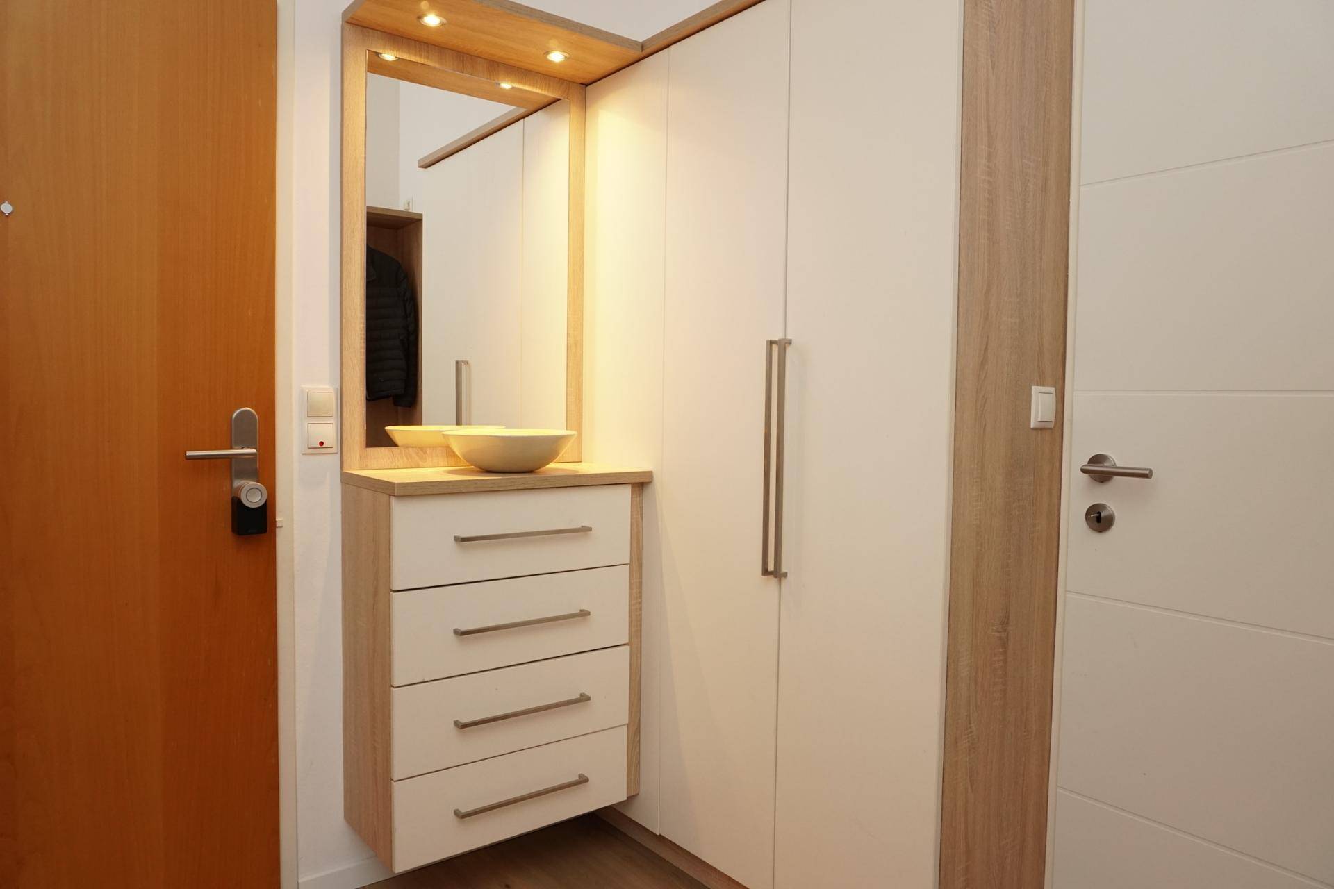 Heller Eingangsbereich mit Einbauschrank, Kommode mit Spiegel und Holzfußboden.