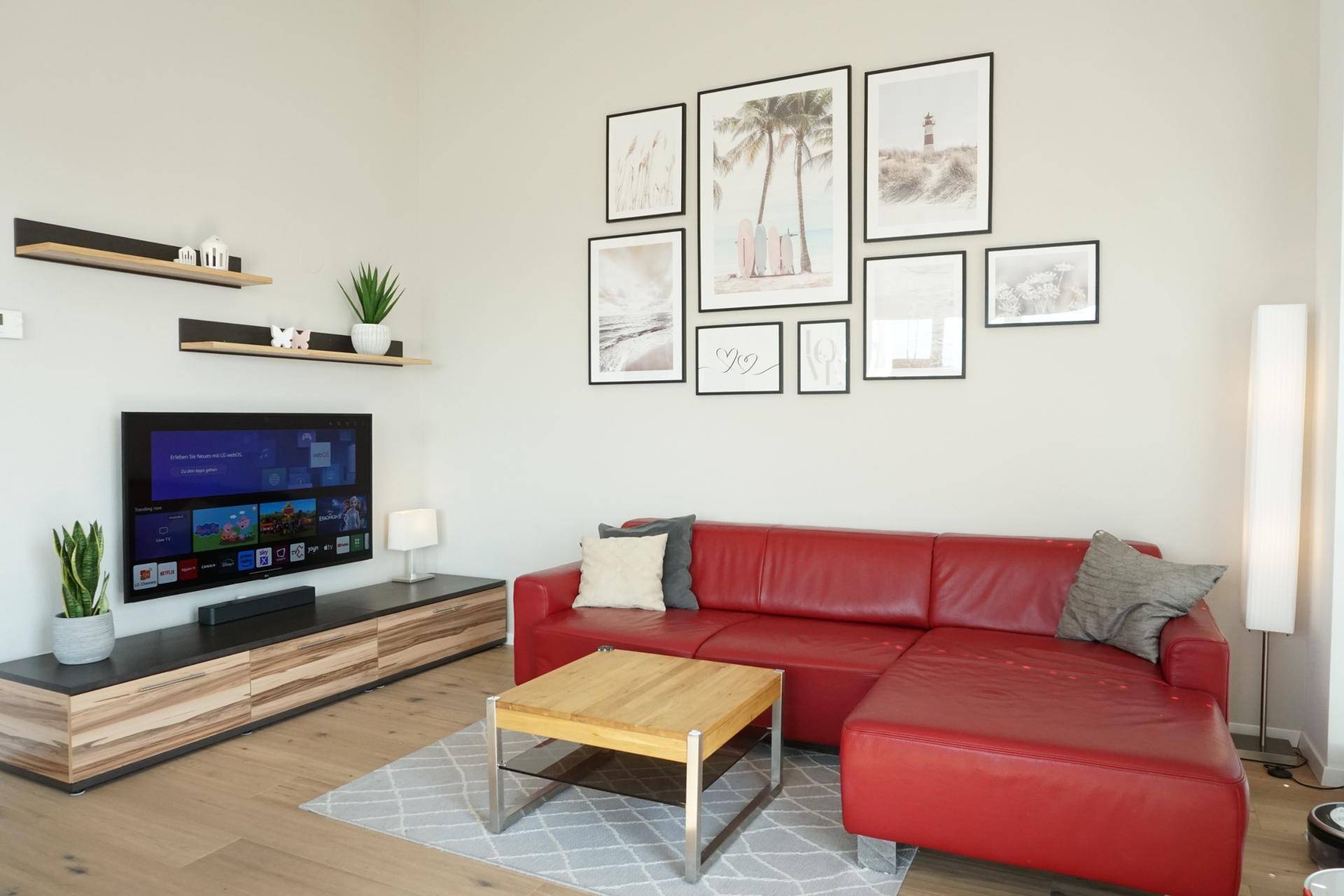 Gemütliches Wohnzimmer mit rotem Ecksofa, Holztisch und moderner Wanddekoration.