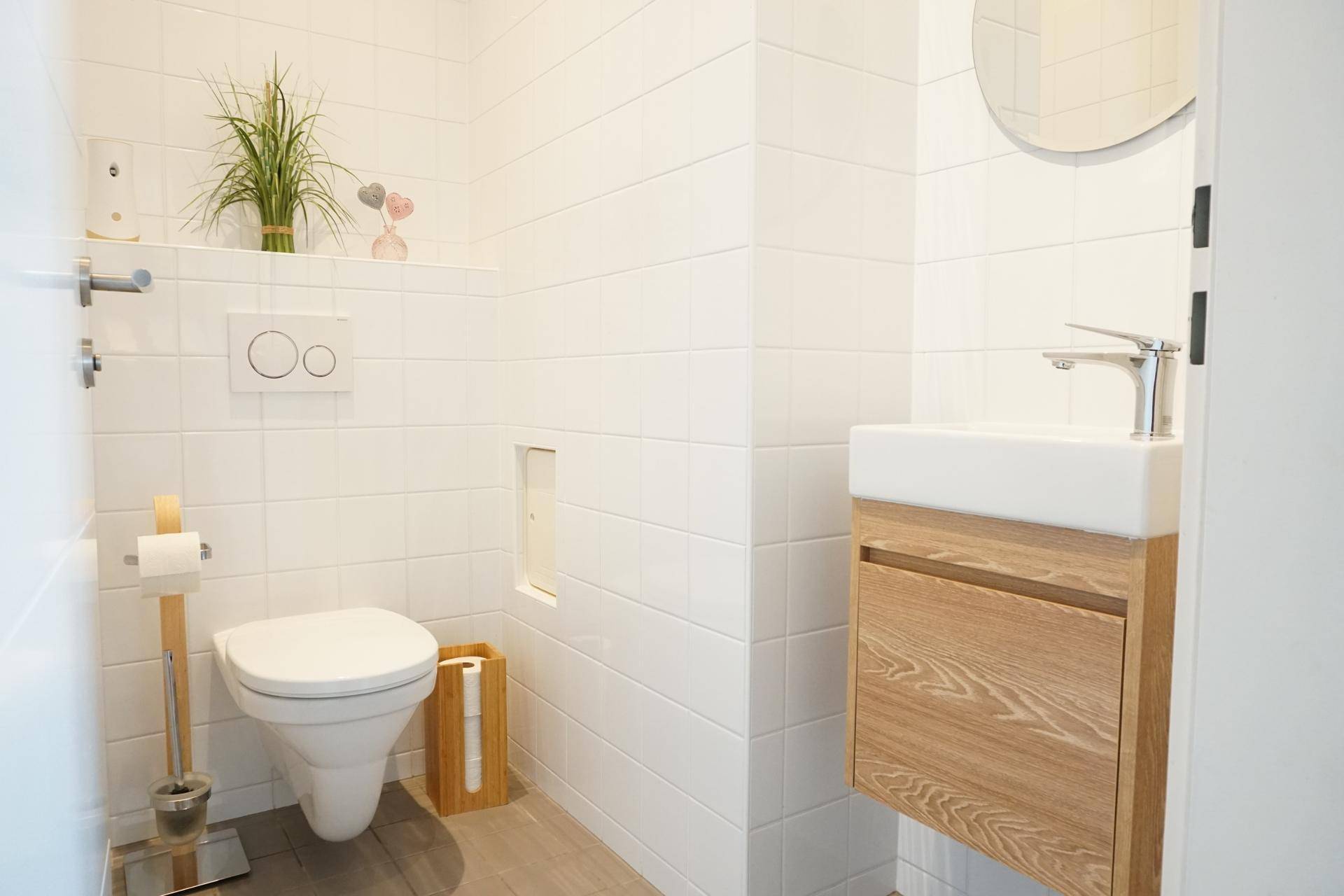 Helles Gäste-WC mit wandhängendem WC, kleinem Waschbecken und modernen Fliesen.