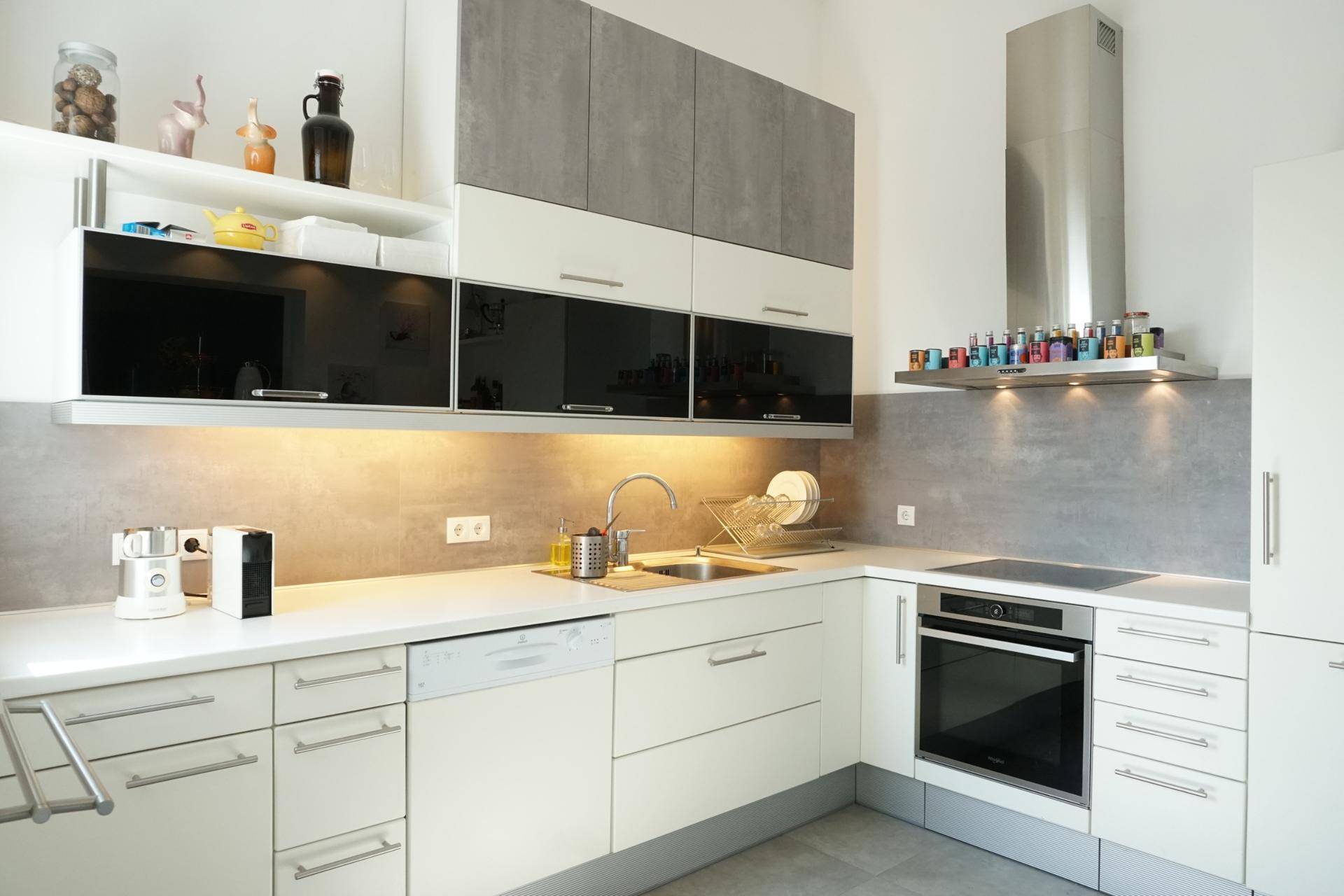 Moderne Einbauküche mit weißen und grauen Fronten, integrierten Geräten und Dunstabzugshaube.