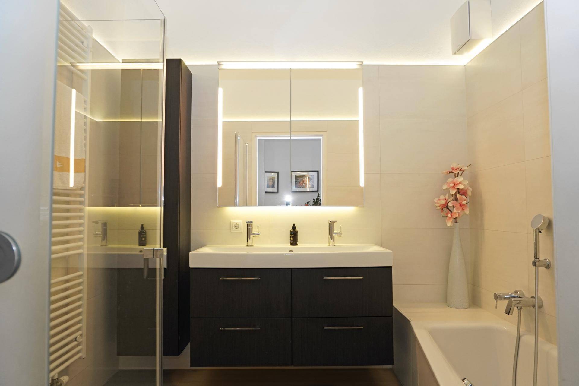 Modernes Badezimmer mit Doppelwaschbecken, beleuchtetem Spiegelschrank und Badewanne.