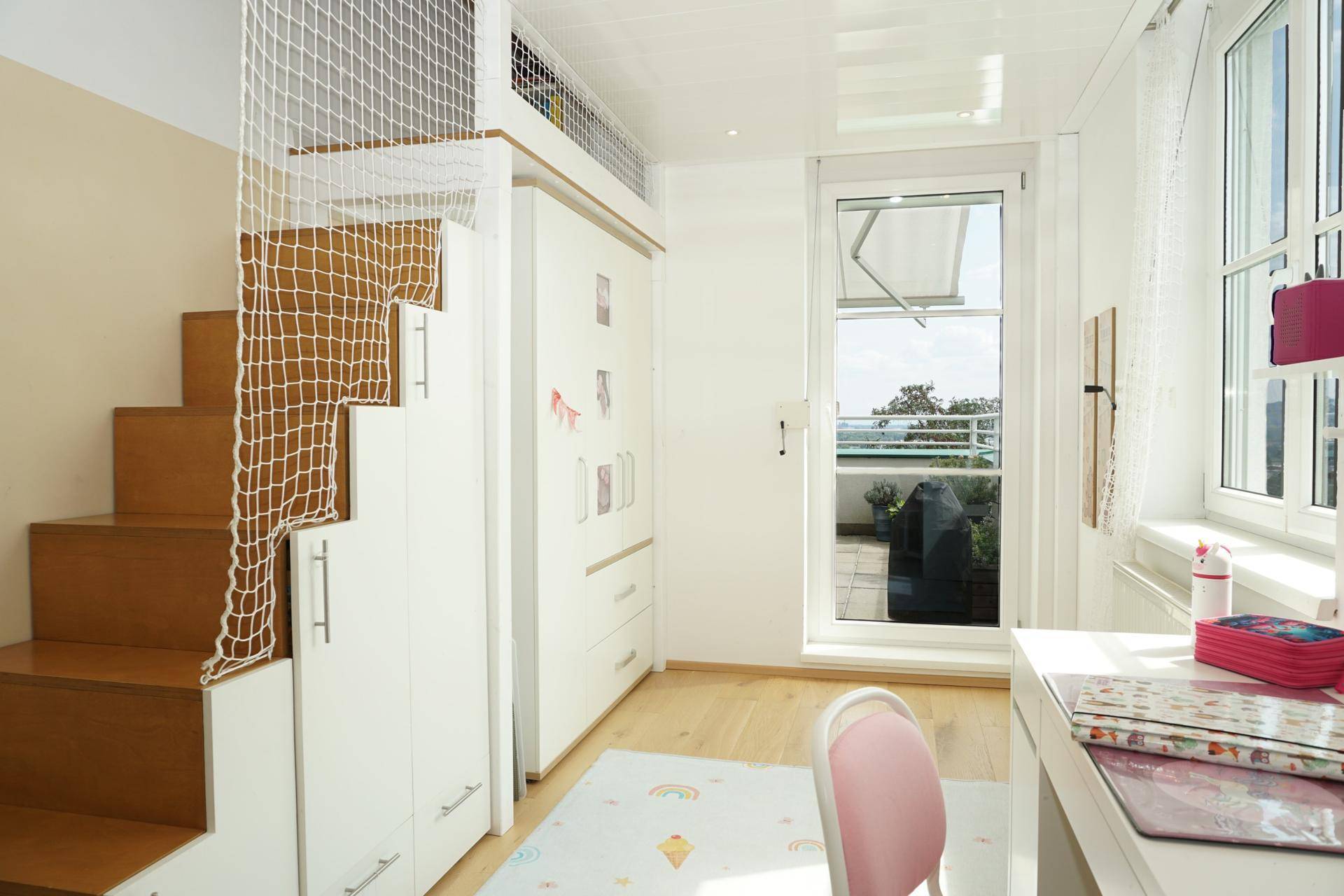 Kinderzimmer mit Schreibtisch, Schrank und Hochbettzugang, mit Blick und Zugang zum Balkon.