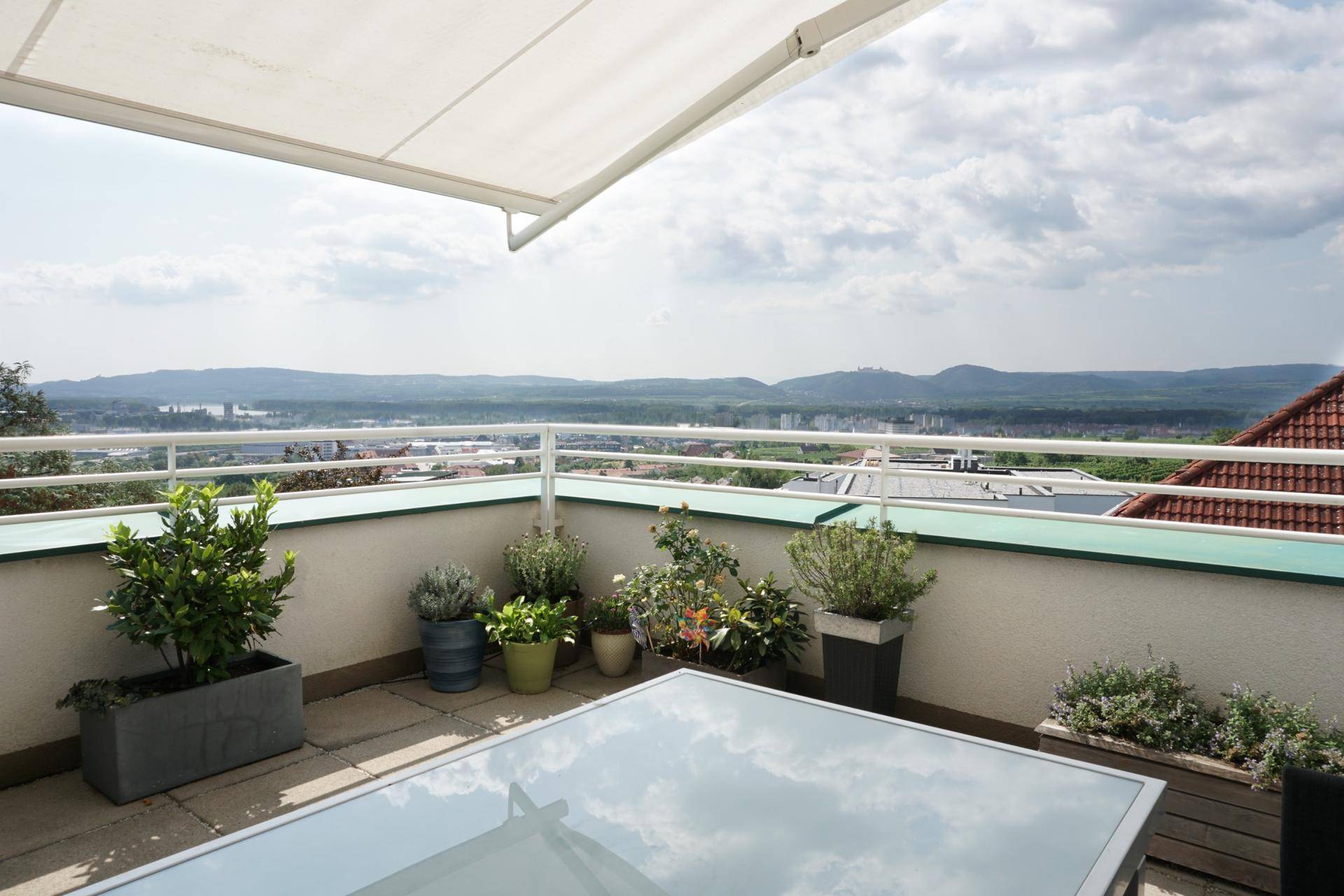 Geräumige Terrasse mit Markise, Pflanzen und weitem Blick über die Stadt und Landschaft.