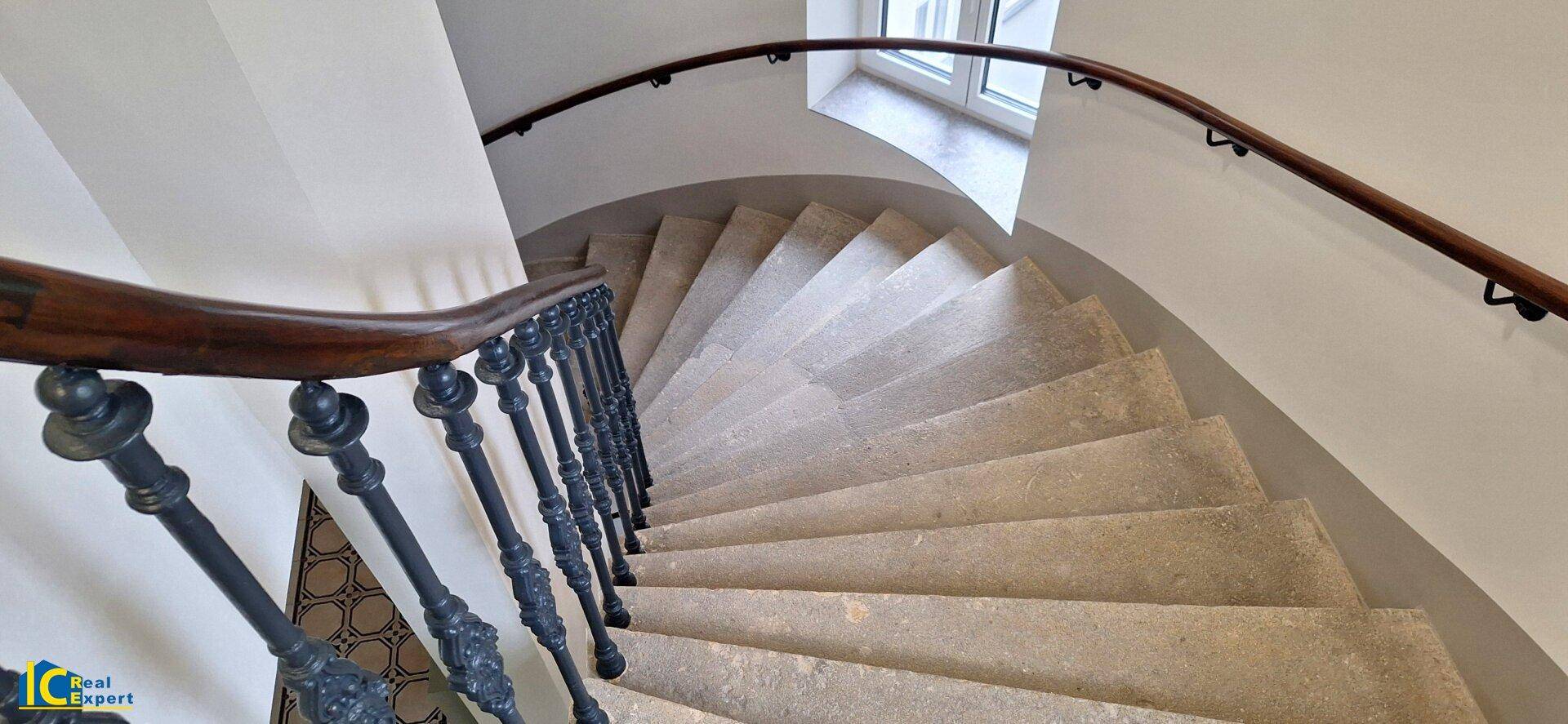 Elegantes Wendeltreppenhaus mit Steinstufen, schmiedeeisernem Geländer und Holzhandlauf.