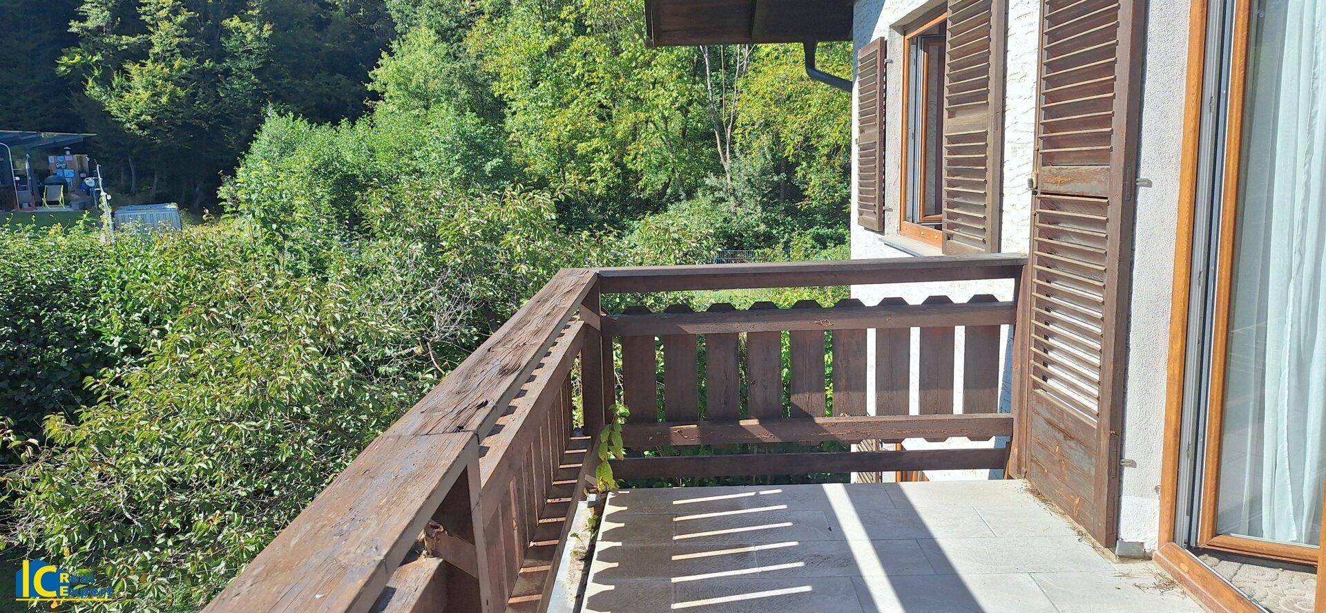 Hölzerner Balkon mit Blick ins Grüne und traditionellem Geländer unter strahlendem Sonnenschein.