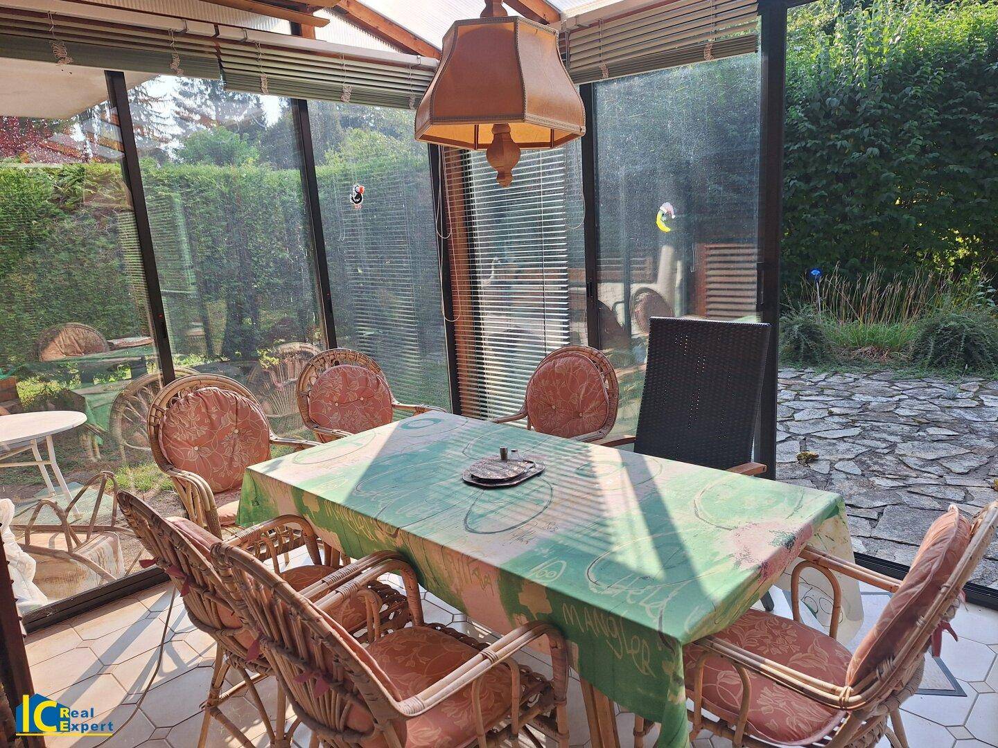 Heller Wintergarten mit Rattanmöbeln und Blick in den grünen Gartenbereich, ideal zum Entspannen.