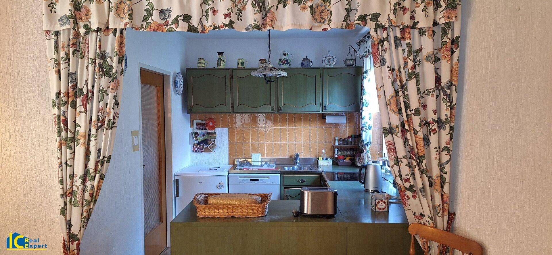 Traditionelle Küche mit grünen Schränken, orangefarbenen Fliesen und praktischer Durchreiche.