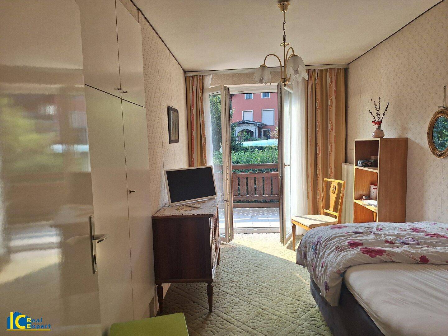 Helles Schlafzimmer mit Balkonzugang, Einzelbett und traditionellen Möbeln, lichtdurchflutet.