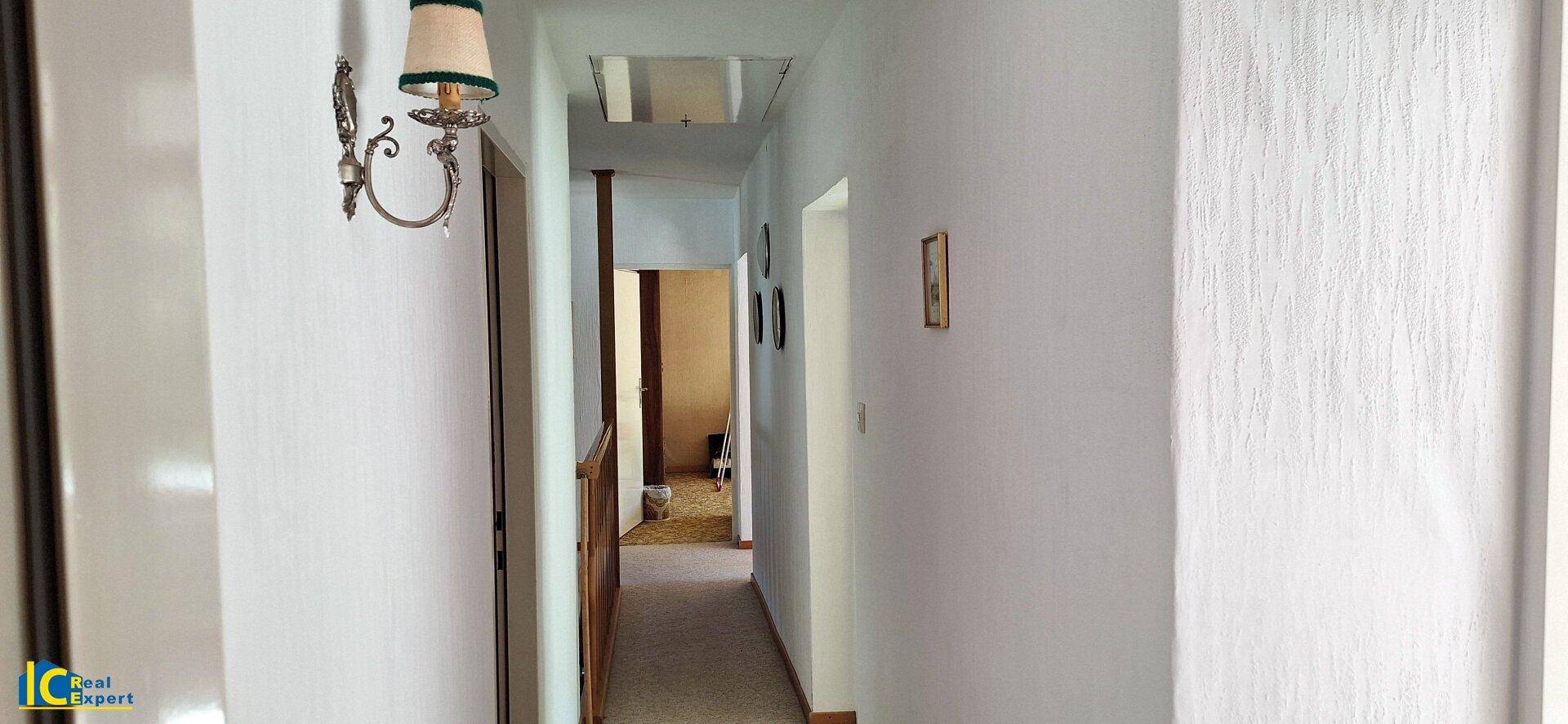 Langer, heller Flur mit Teppichboden und Zugang zu weiteren Räumen, gut beleuchtet.
