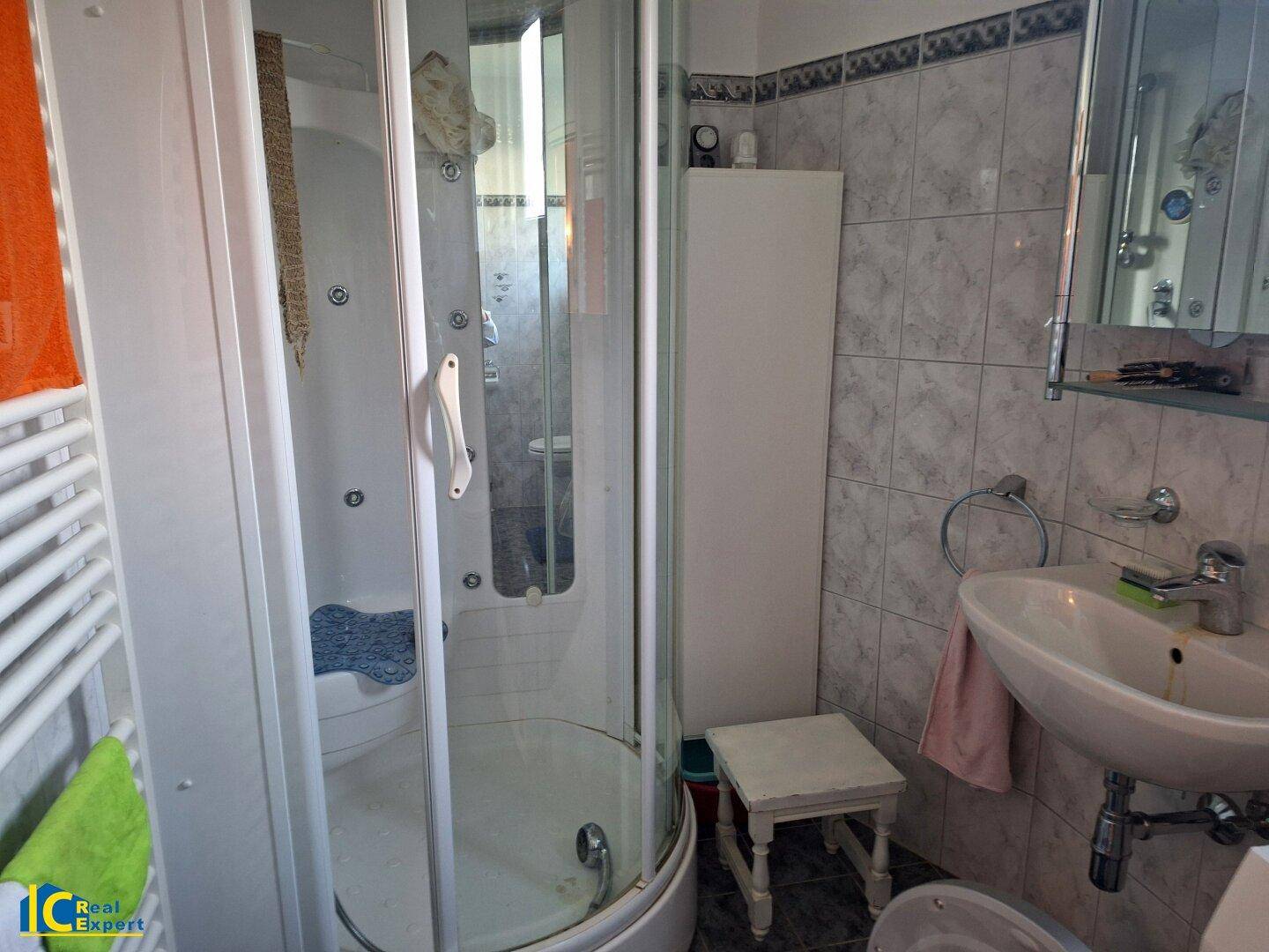 Kleines Badezimmer mit Duschkabine, Waschbecken und beheiztem Handtuchhalter, funktional eingerichtet.