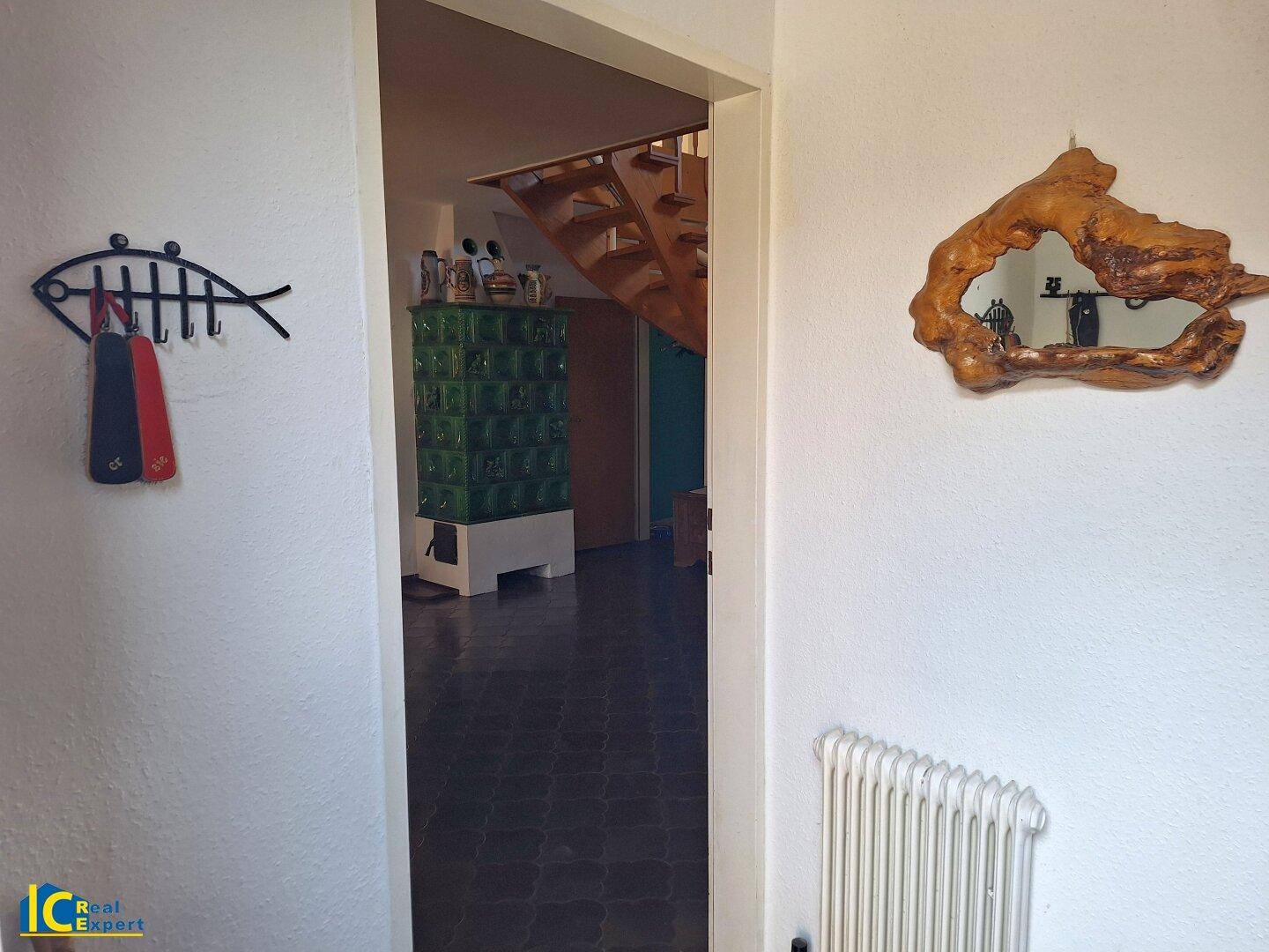 Eingangsbereich mit Kachelofen, dunklen Fliesen und rustikaler Wanddekoration, einladend und warm.