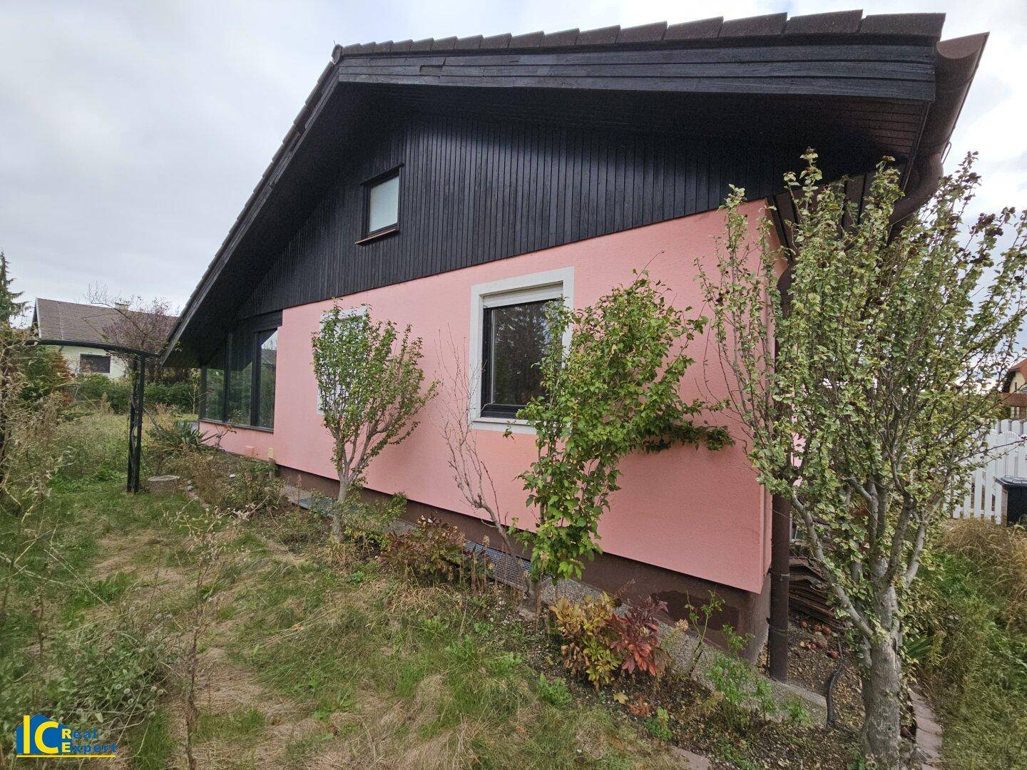 Seitenansicht des Hauses mit rosafarbener Fassade und dunkler Holzverkleidung unter dem Dachgiebel.