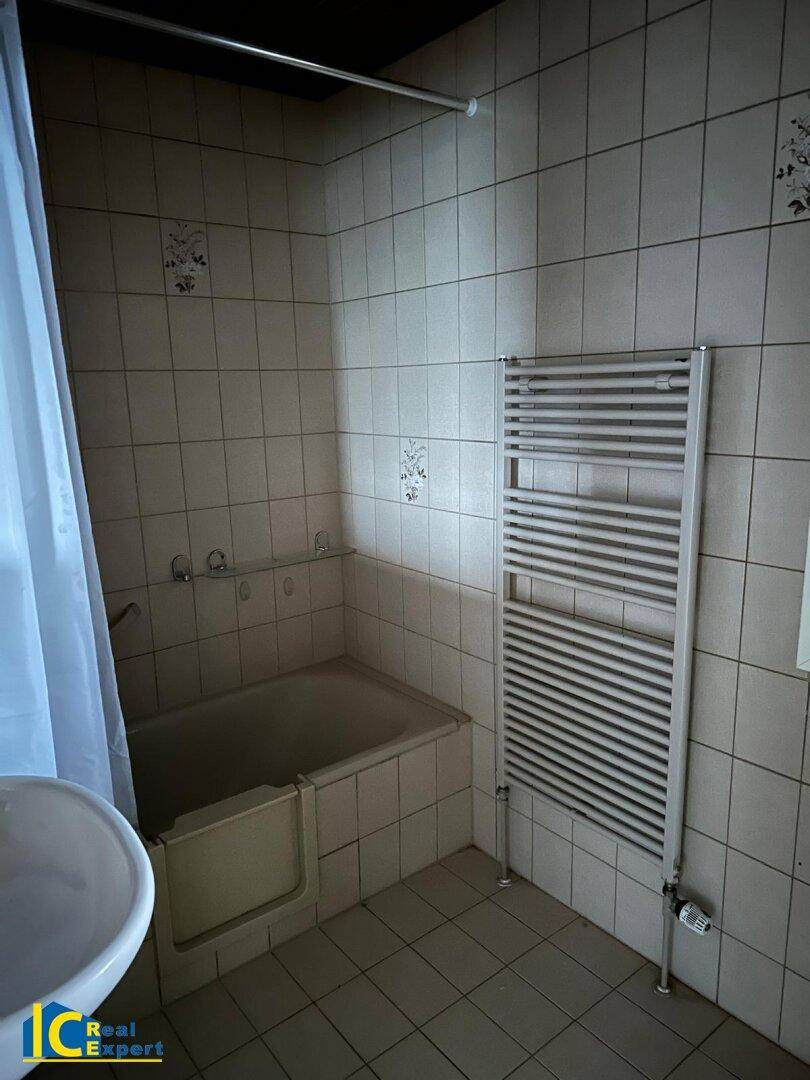 Badezimmer mit Badewanne, weißen Fliesen und praktischem beheiztem Handtuchhalter.