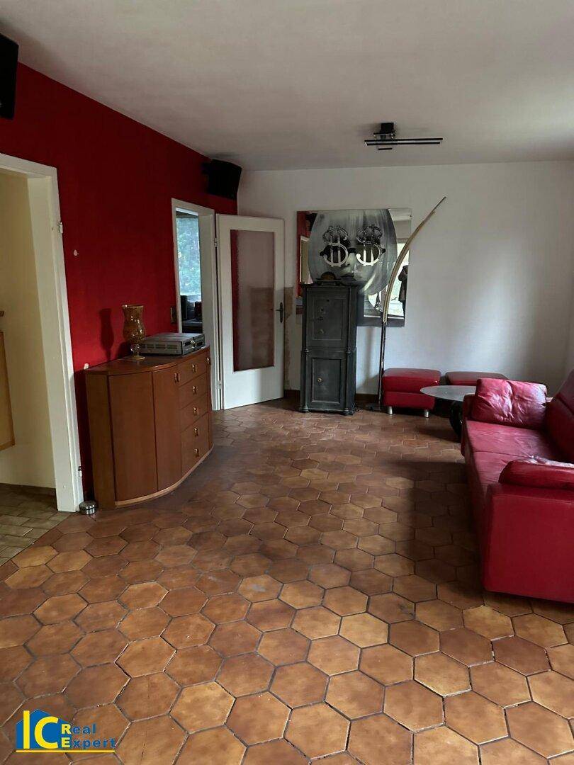 Geräumiges Wohnzimmer mit roter Akzentwand, Terrakottafliesen und bequemer roter Couch.