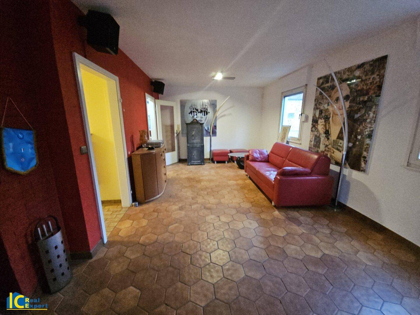 Weitläufiges Wohnzimmer mit Terrakottafliesen, roter Wand und moderner Kunstdekoration.