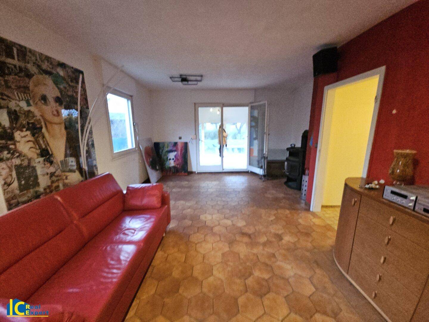 Helles Wohnzimmer mit Terrakottafliesen, roter Couch und Zugang zum Wintergarten.
