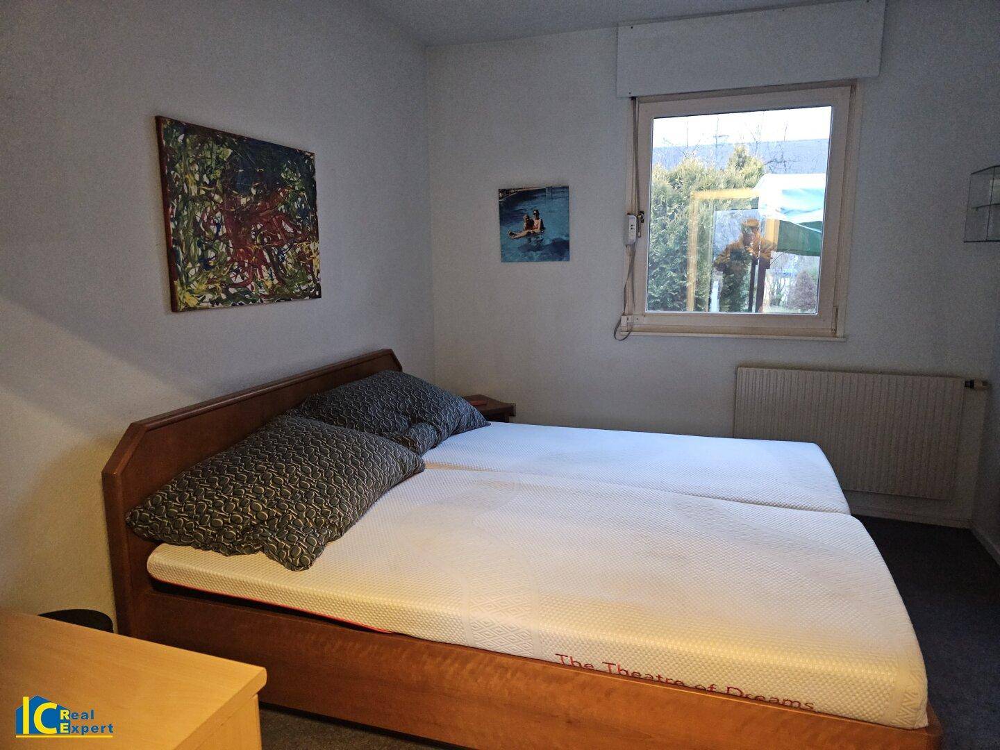 Schlafzimmer mit Doppelbett, Teppichboden und Fenster mit Blick ins Grüne.