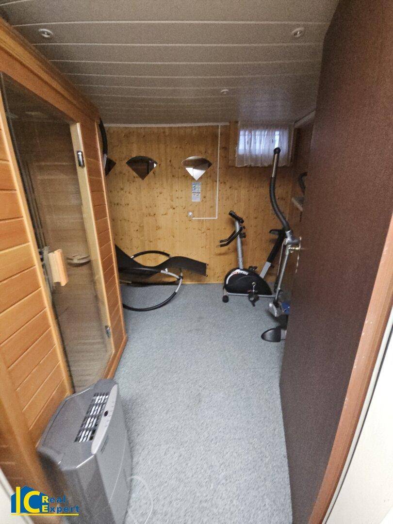 Fitnessraum im Keller mit Sauna, Trainingsgeräten und Holzverkleidung für Wellness und Sport.