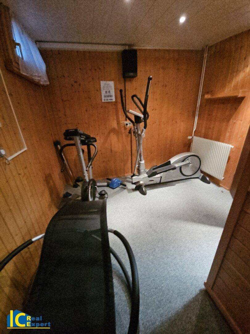 Gut ausgestatteter Fitnessraum mit verschiedenen Trainingsgeräten und Holzverkleidung.