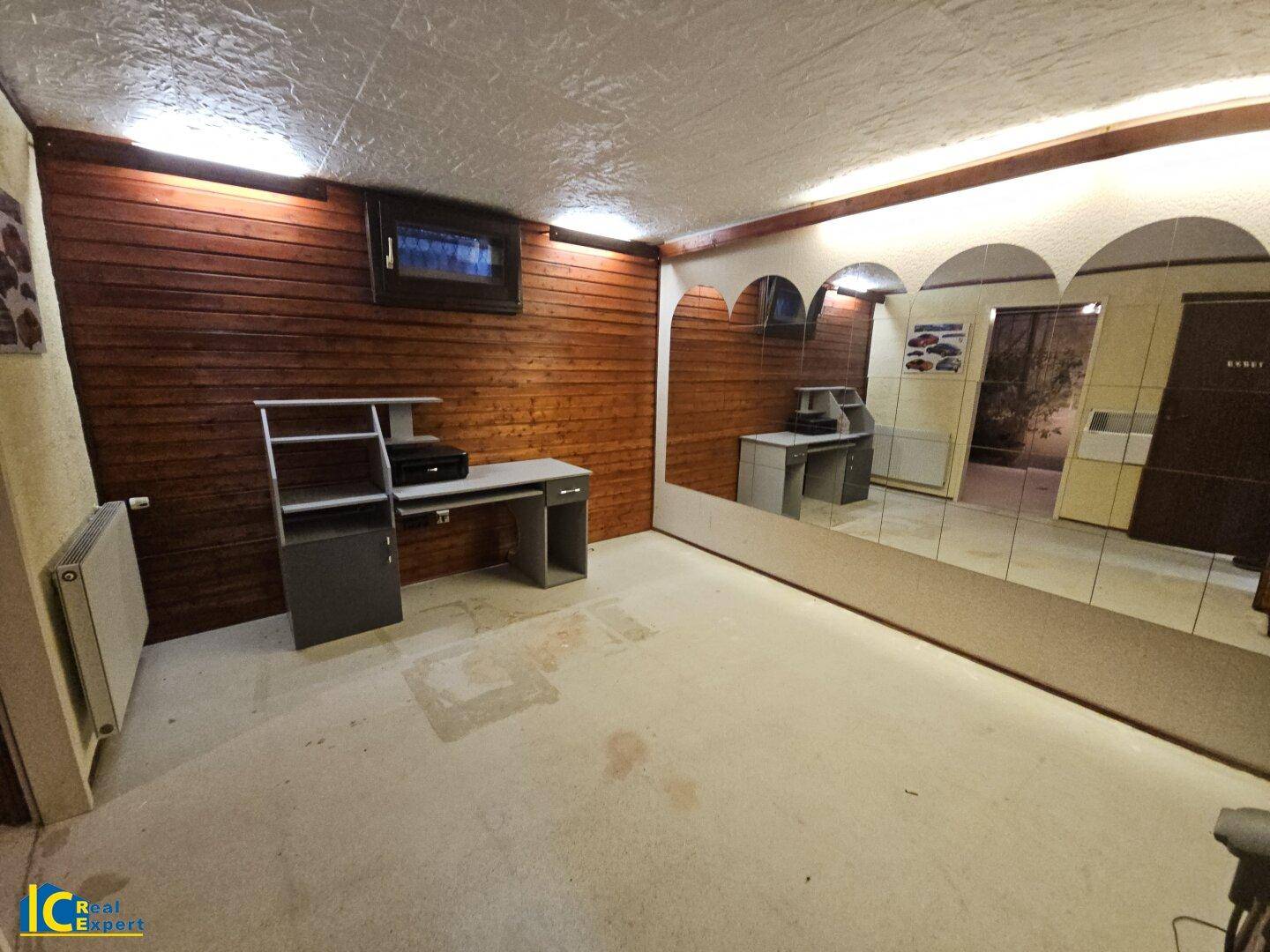 Vielseitiger Raum mit Holzvertäfelung, Schreibtisch und großer Spiegelwand, nutzbar als Büro oder Hobbyraum.
