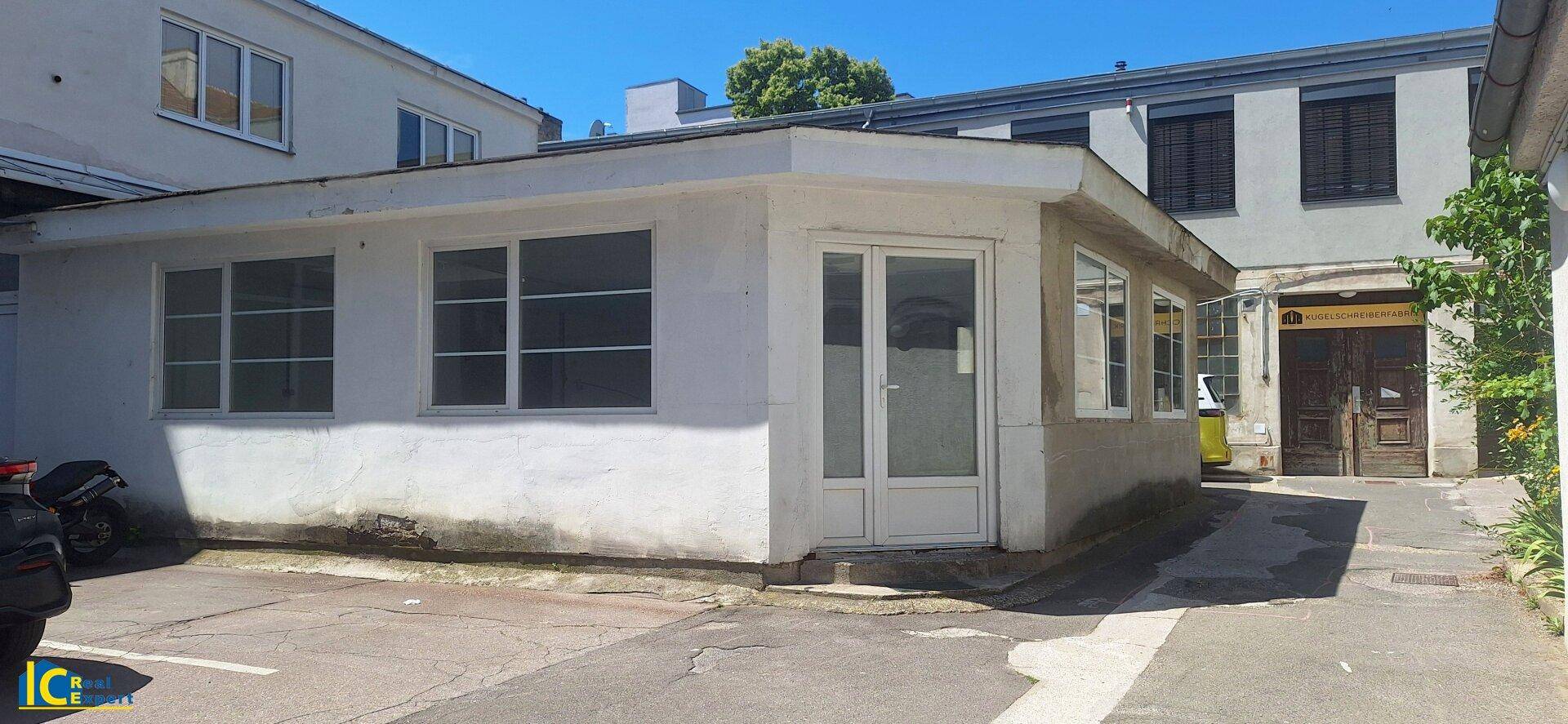 Außenansicht des kleinen Gebäudes mit Eingangstür und Fenstern in einem gepflasterten Innenhof.