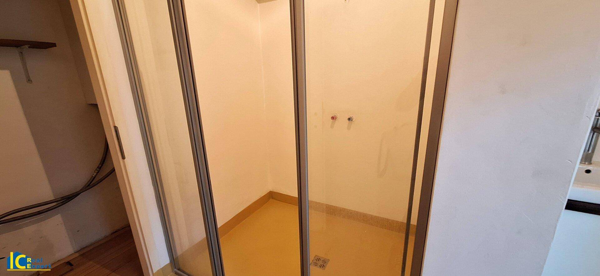 Duschkabine mit Glastüren und gelb gefliestem Boden, in einem schlichten Badezimmerbereich.
