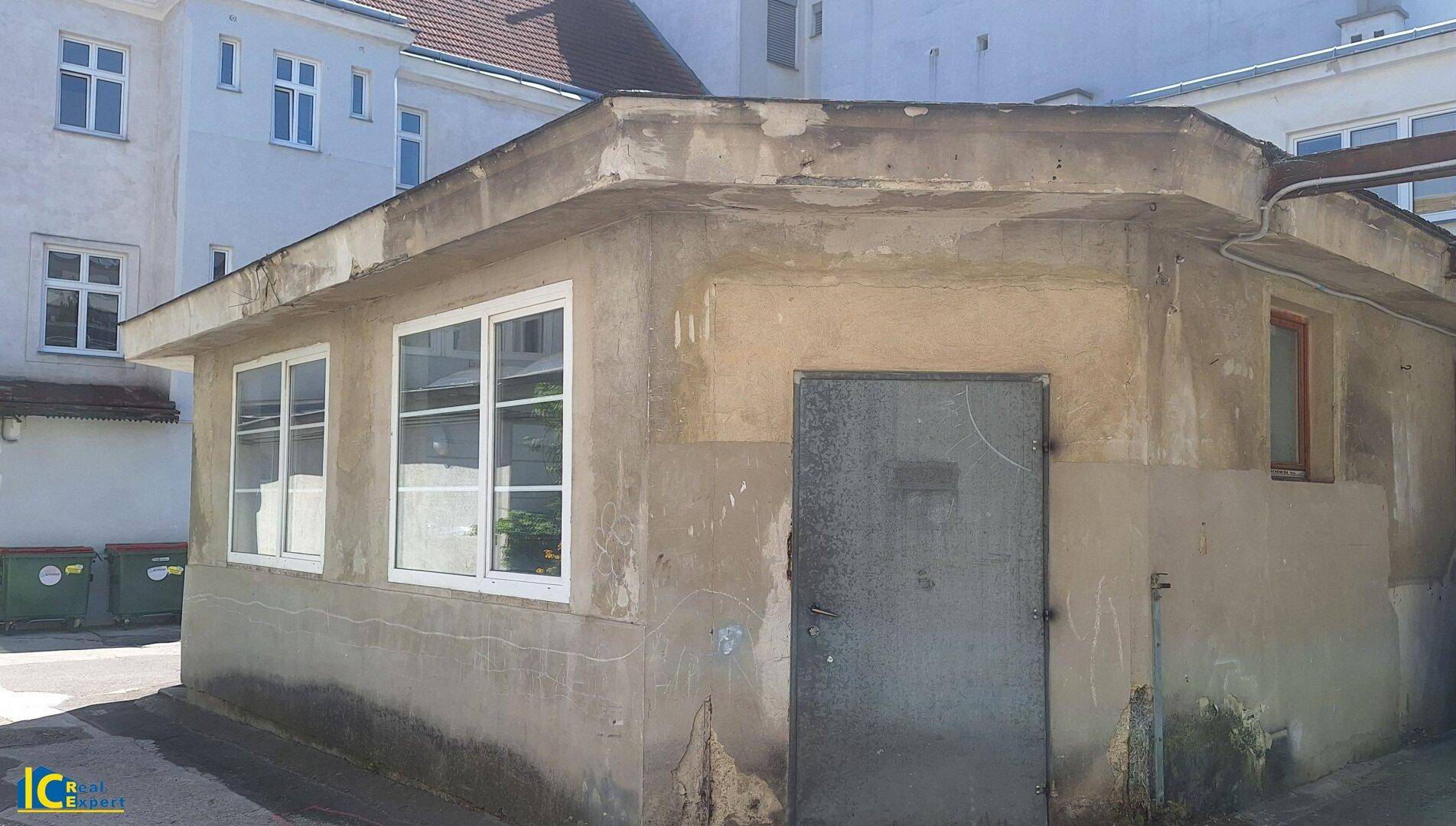 Seitenansicht des kleinen Gebäudes mit einer Metalltür und rauen, ungestrichenen Wänden.