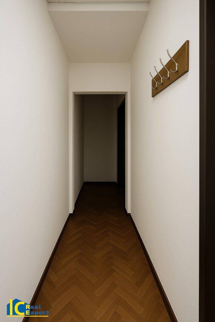 Schmaler Flur mit Fischgrätparkett und einer Garderobenleiste an der weißen Wand.