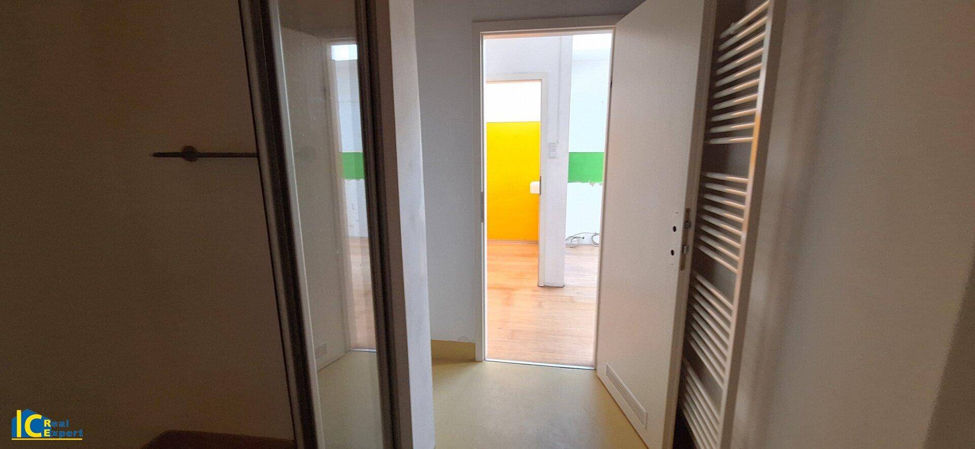 Blick durch eine Tür in einen Flur, der zu einem Raum mit gelben Wänden führt.