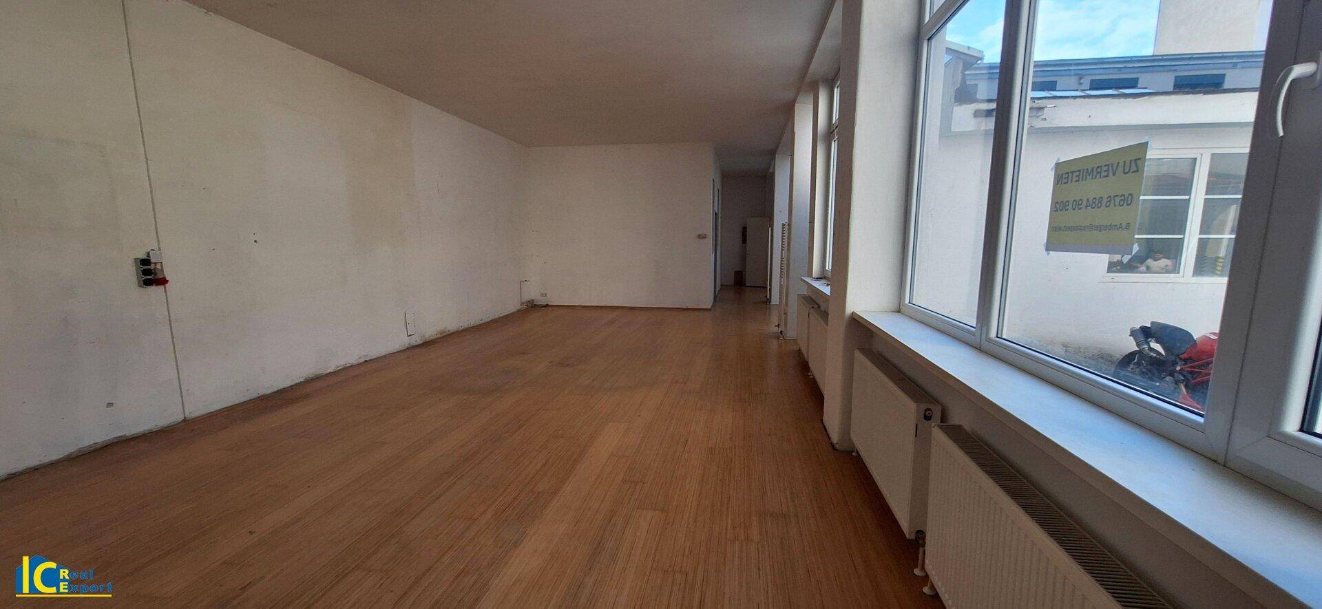 Langer, heller Raum mit Holzplankenboden und einer Fensterfront, die viel Tageslicht hereinlässt.