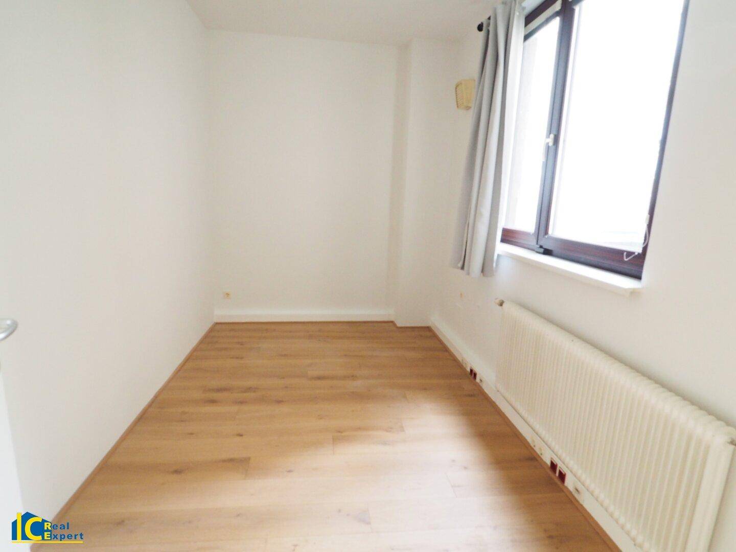 Kleiner, heller Raum mit hellem Holzfußboden, weiß gestrichenen Wänden und einem Fenster.