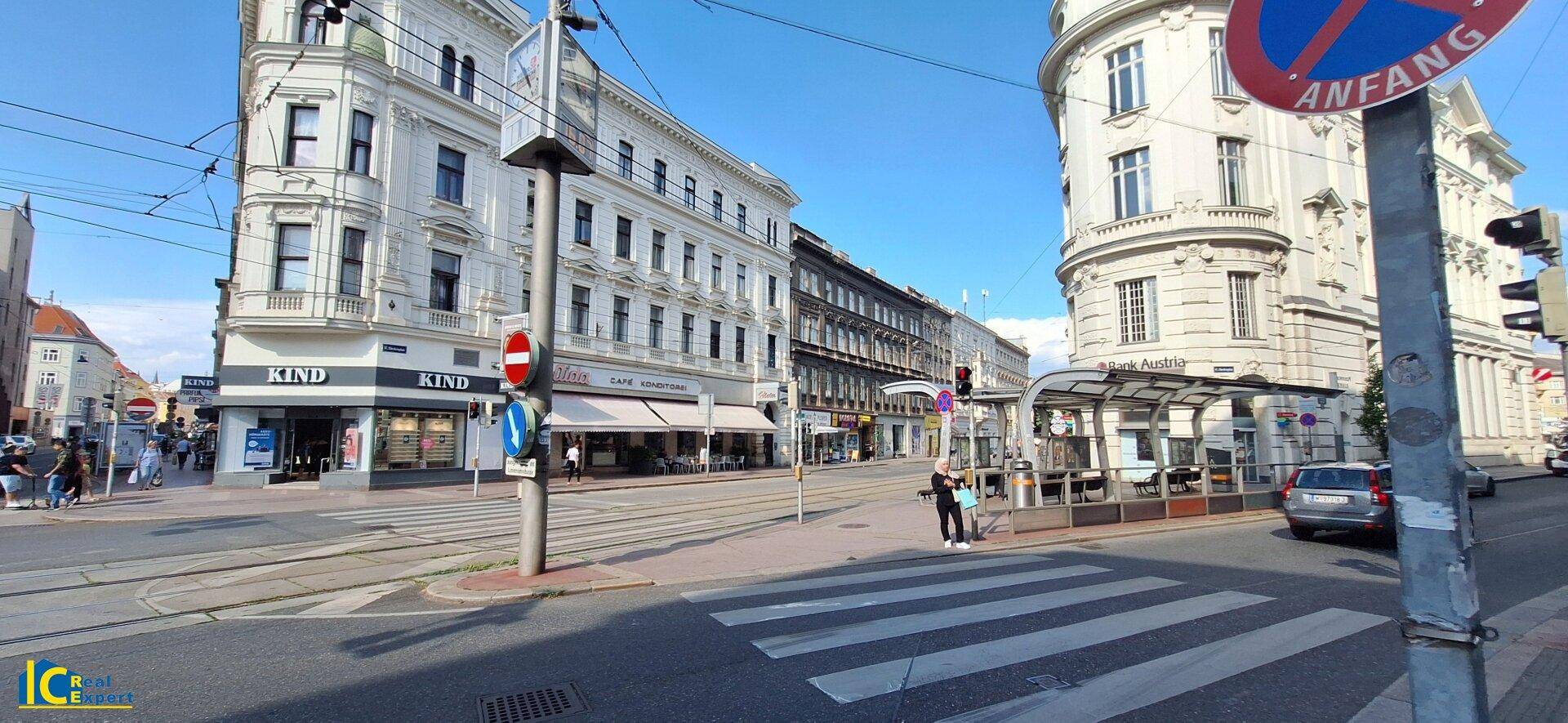 Straßenansicht einer städtischen Gegend mit historischen Gebäuden, einer Straßenbahnhaltestelle und Verkehrsschildern.