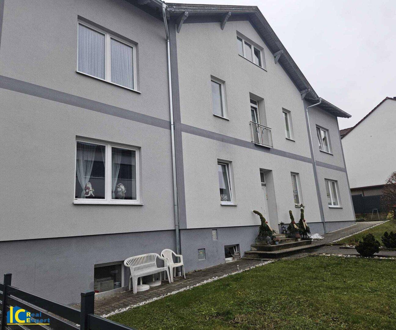 Detailansicht der Fassade des grauen Wohnhauses mit Fenstern, kleinem Balkon und grünem Rasen.