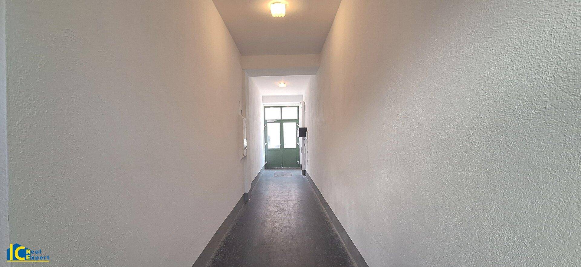 Langer, schmaler Flur mit dunklem Boden und einer Tür am Ende, typisch für ein Mehrfamilienhaus.