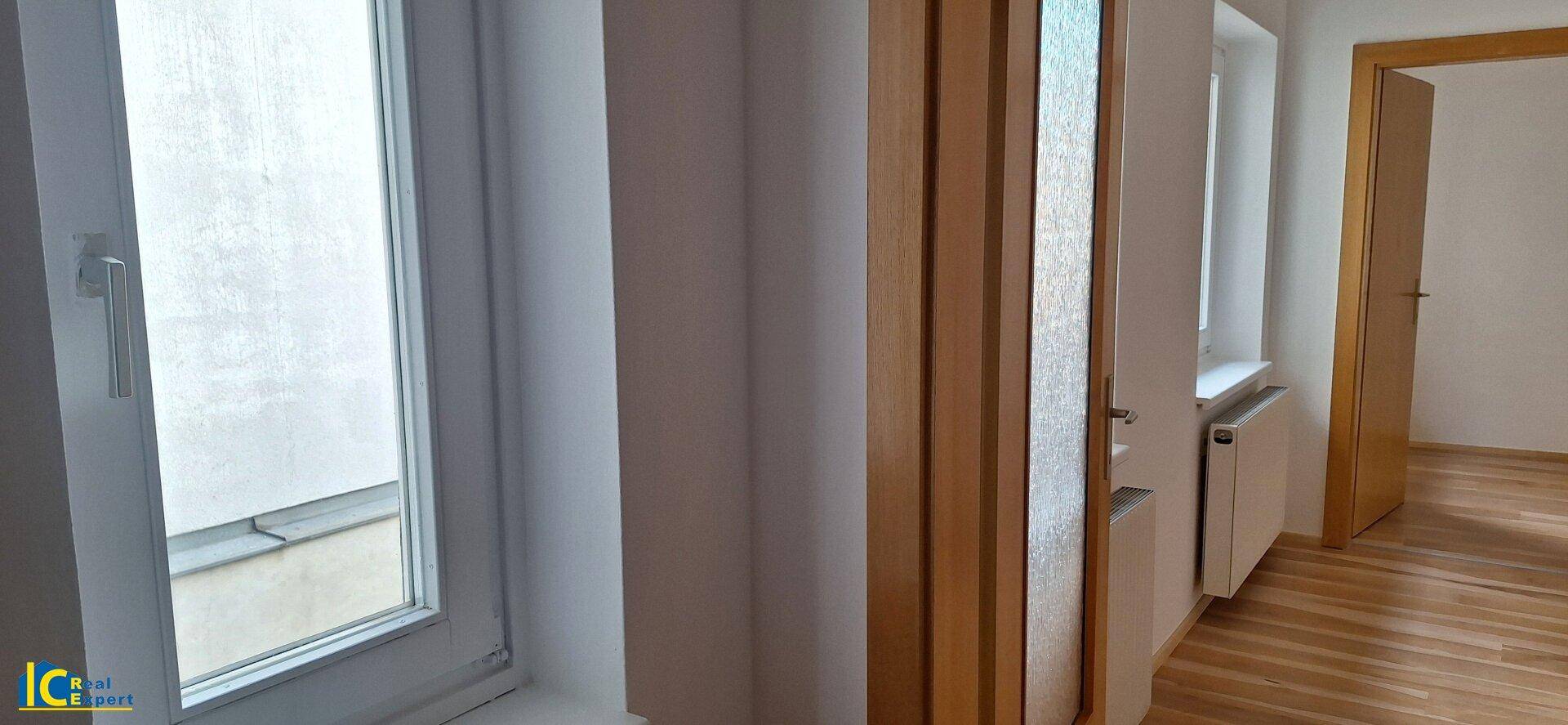 Heller Flur mit Fenstern und Holztüren, der verschiedene Bereiche verbindet.