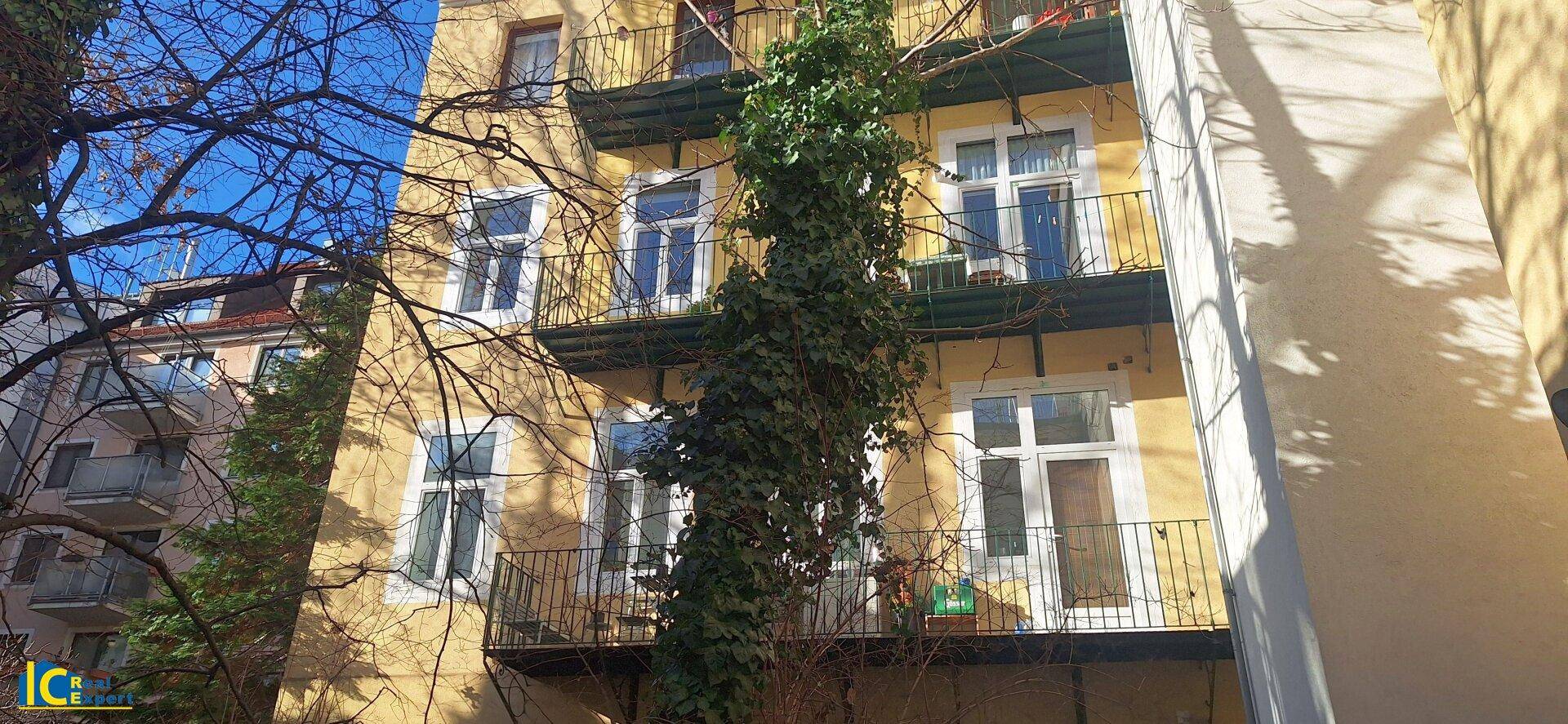 Gelbe Fassade eines Mehrfamilienhauses mit Balkonen und Kletterpflanzen unter blauem Himmel.