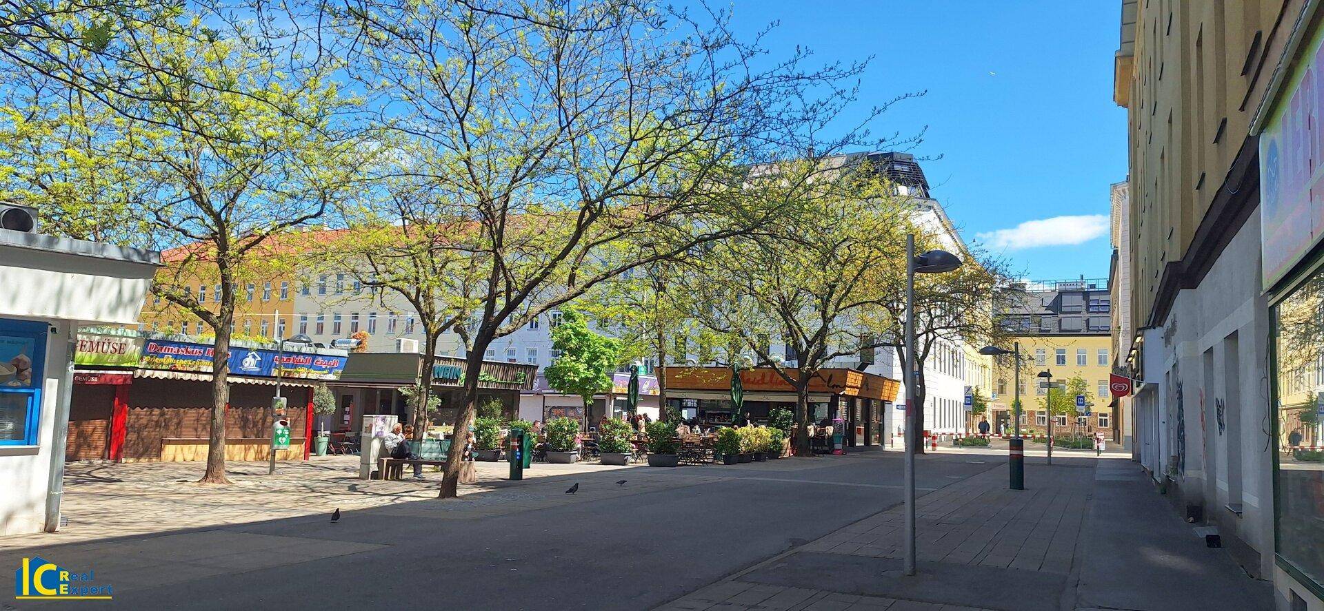 Belebtes Stadtviertel mit Geschäften, Bäumen und sonnigem Wetter.