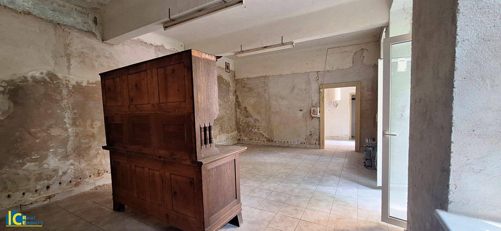 Großer, sanierungsbedürftiger Raum mit Fliesenboden und Zugang zu weiteren Zimmern.