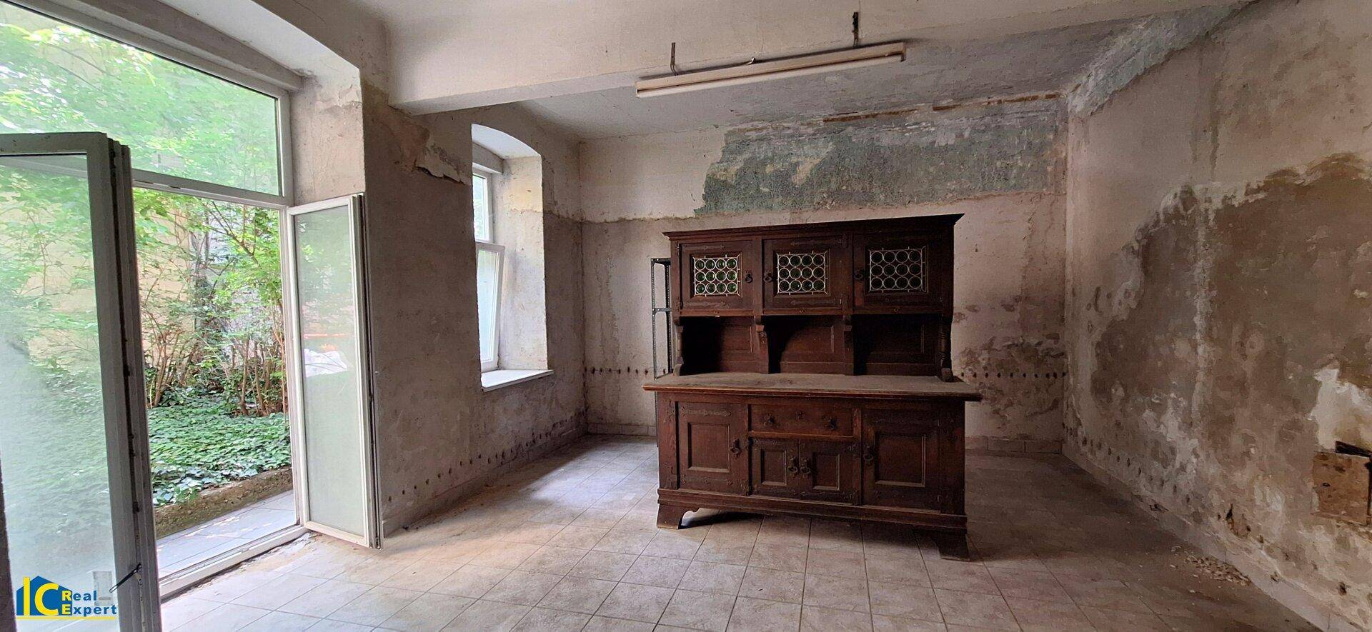 Renovierungsbedürftiger Raum mit altem Holzschrank und Blick in den grünen Innenhof.