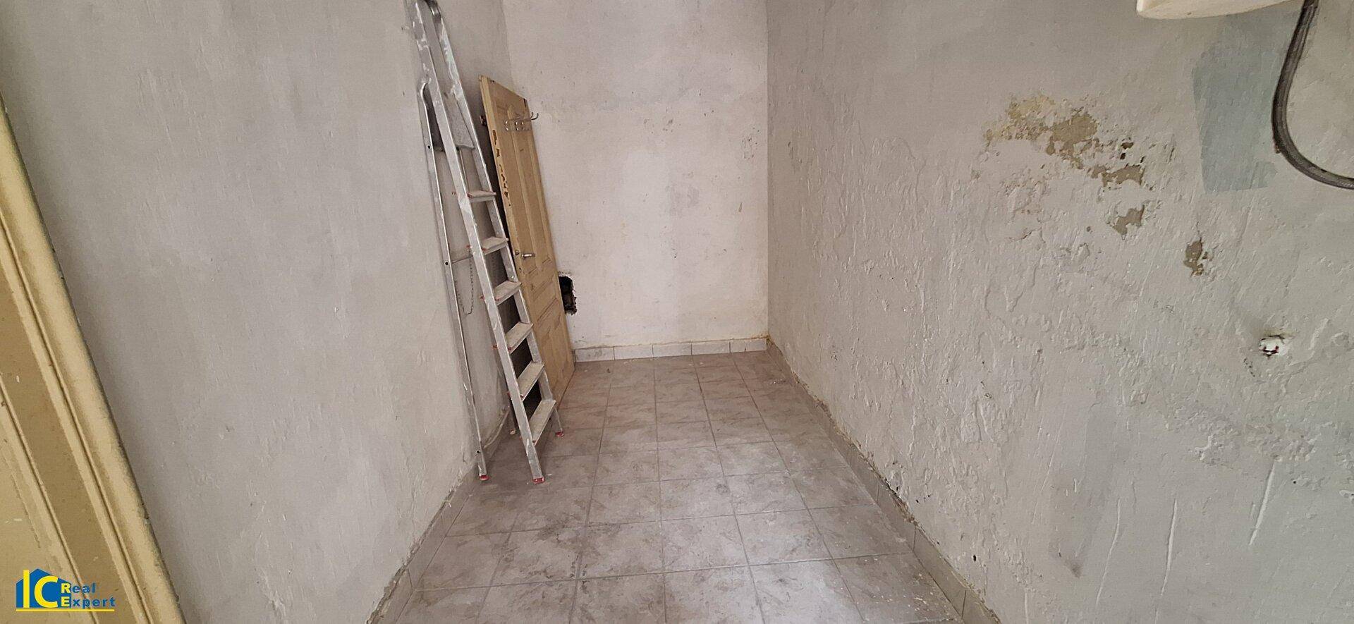 Kleiner, leerer Raum mit Fliesenboden und einer Leiter, benötigt Renovierung.